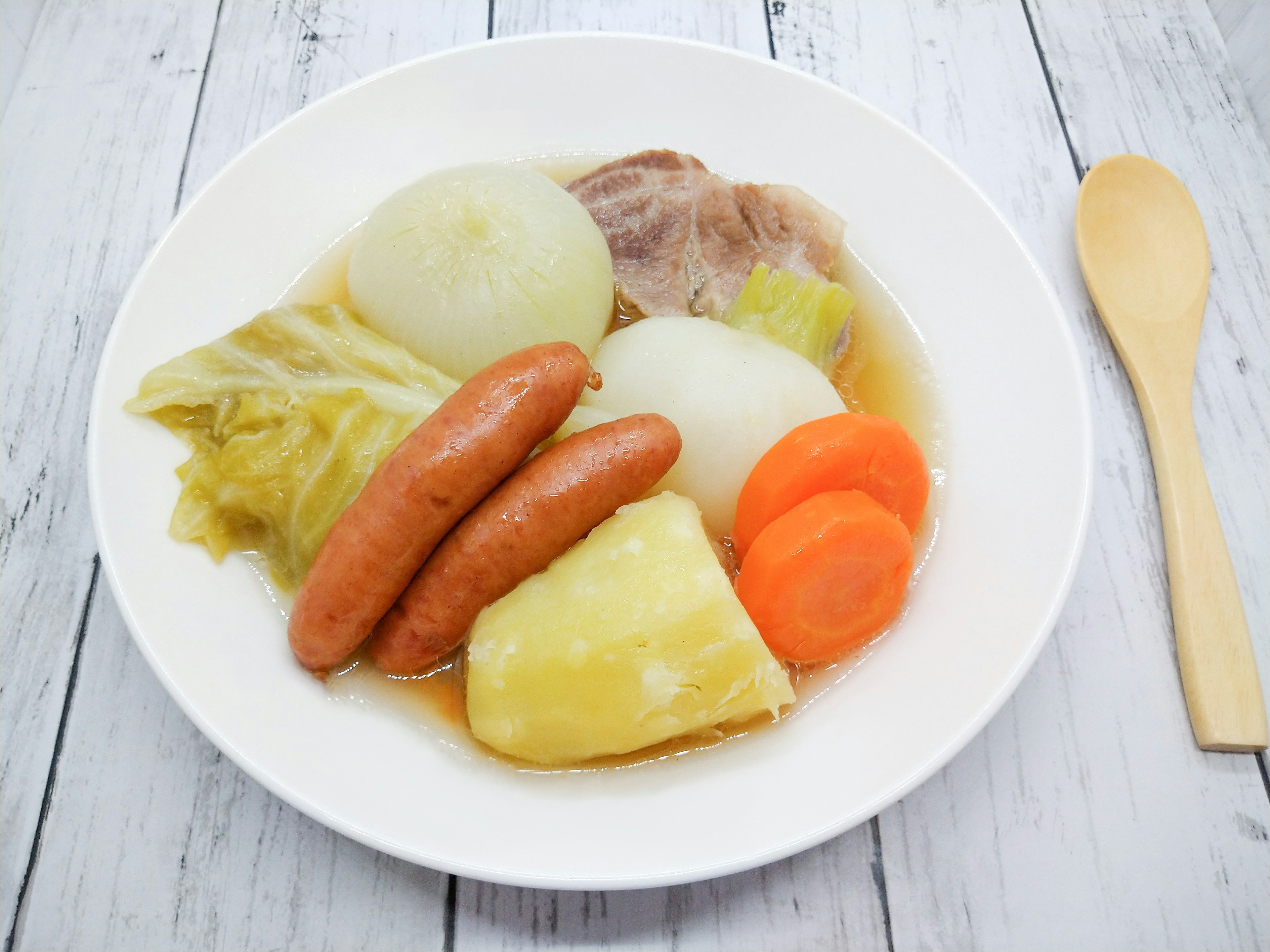 A white bowl filled with vegetable soup featuring sausages and assorted vegetables