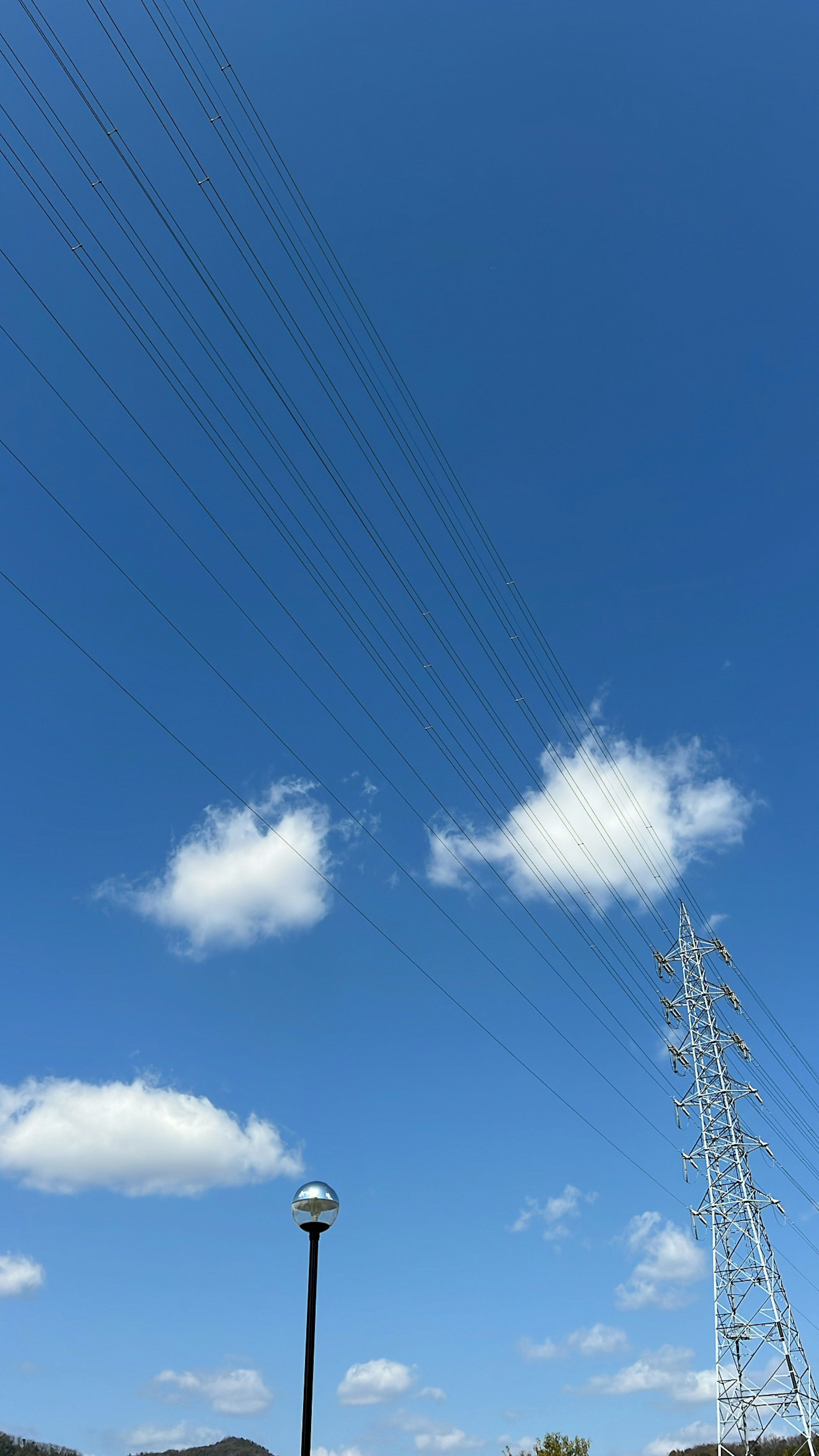 Clear blue sky with white clouds visible power lines and a street lamp