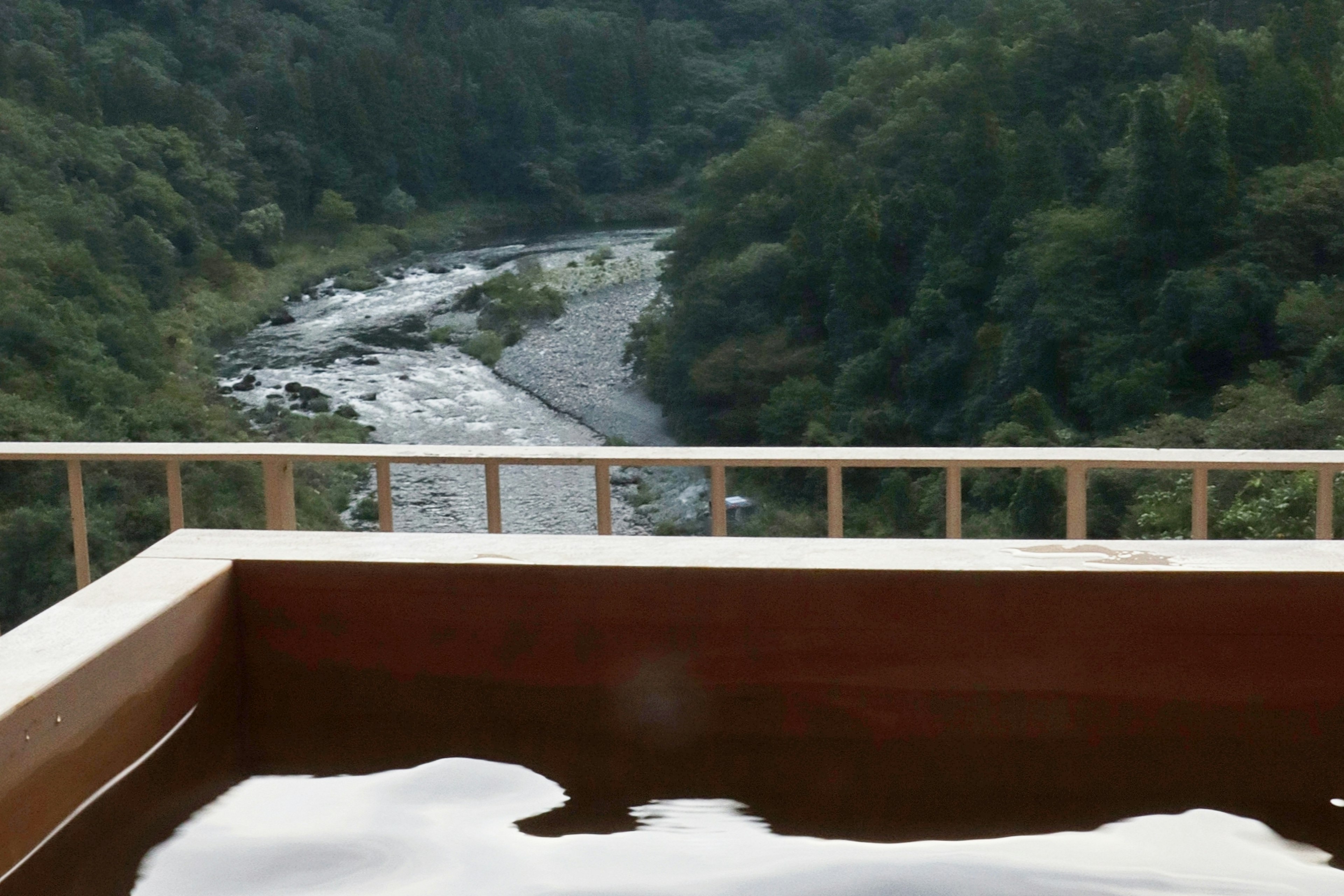 Wooden hot spring tub overlooking a river and green mountains