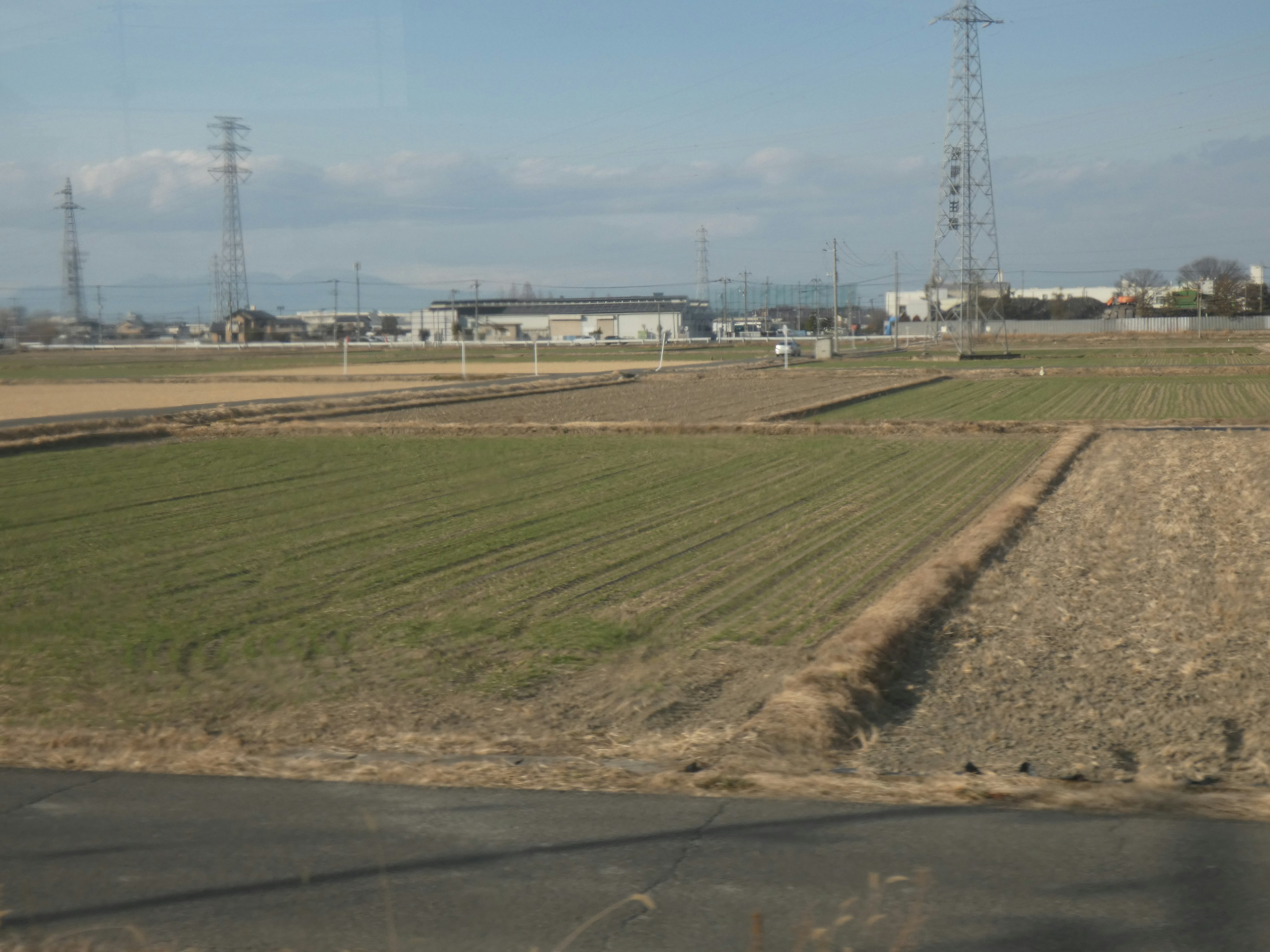 Paysage avec des champs de riz verts et des terres sèches sous un ciel bleu avec des nuages légers et des lignes électriques