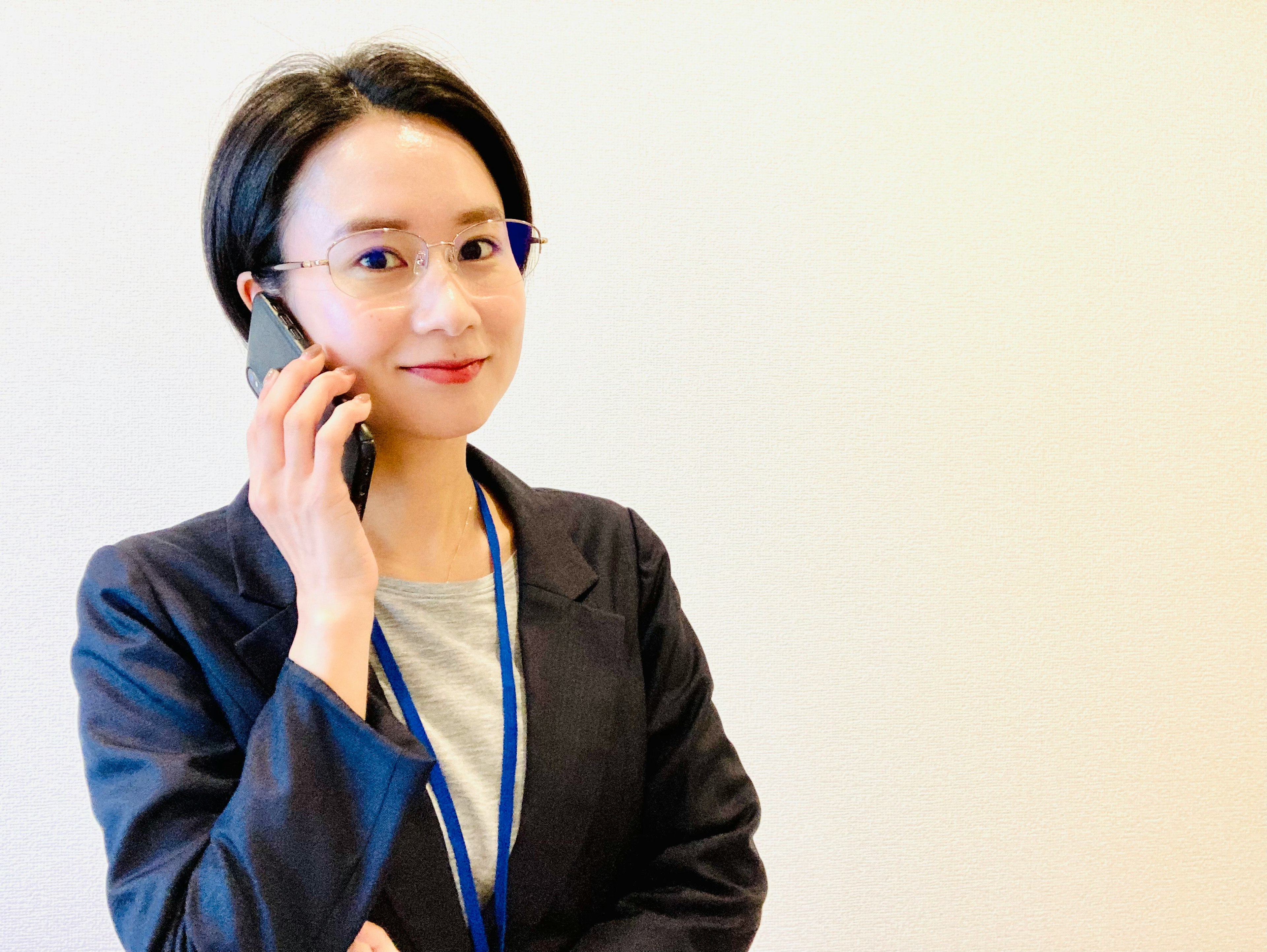 Femme d'affaires au téléphone portant un blazer noir et une cravate bleue avec un fond de bureau moderne