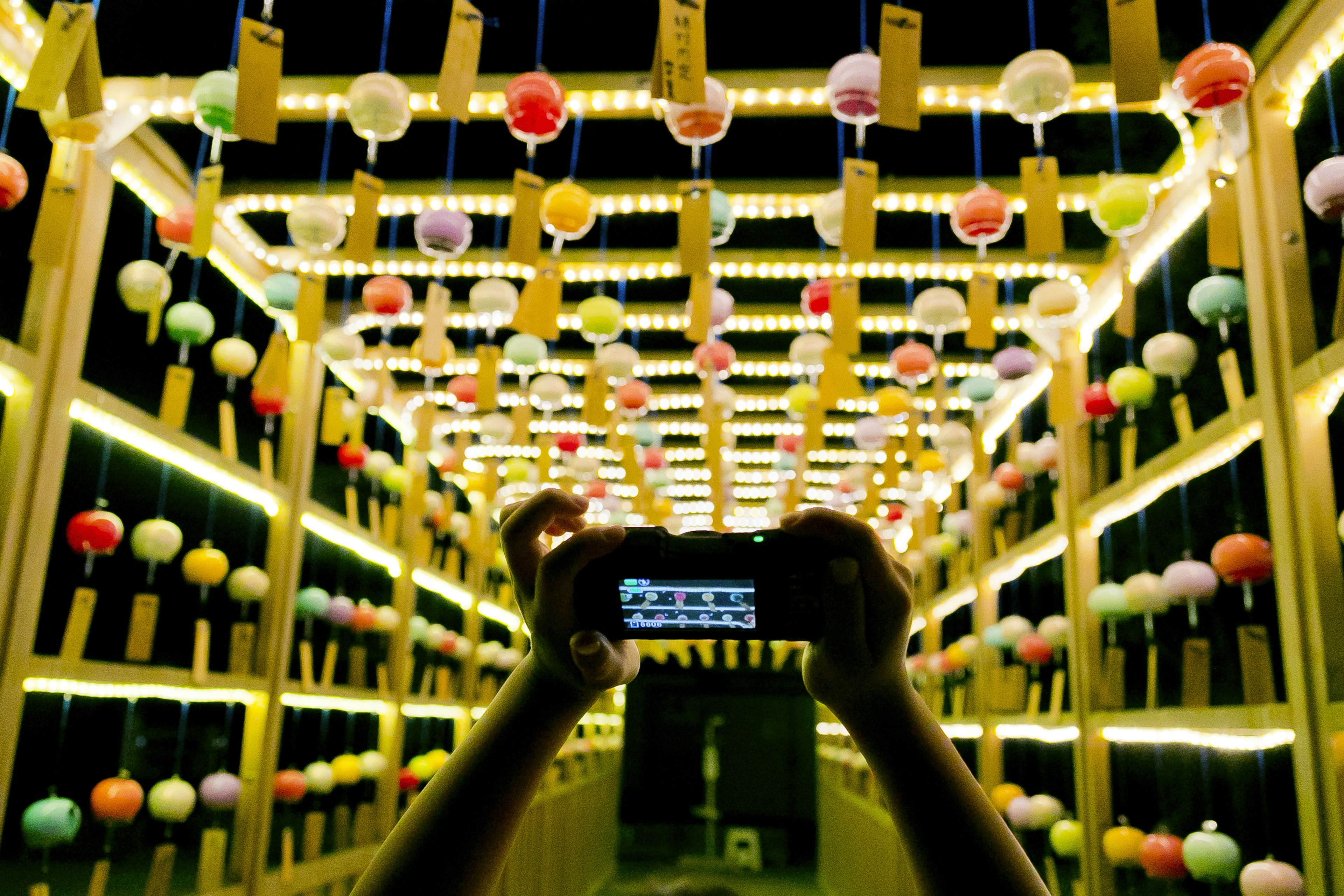 A hand holding a smartphone in a dark corridor adorned with colorful lanterns