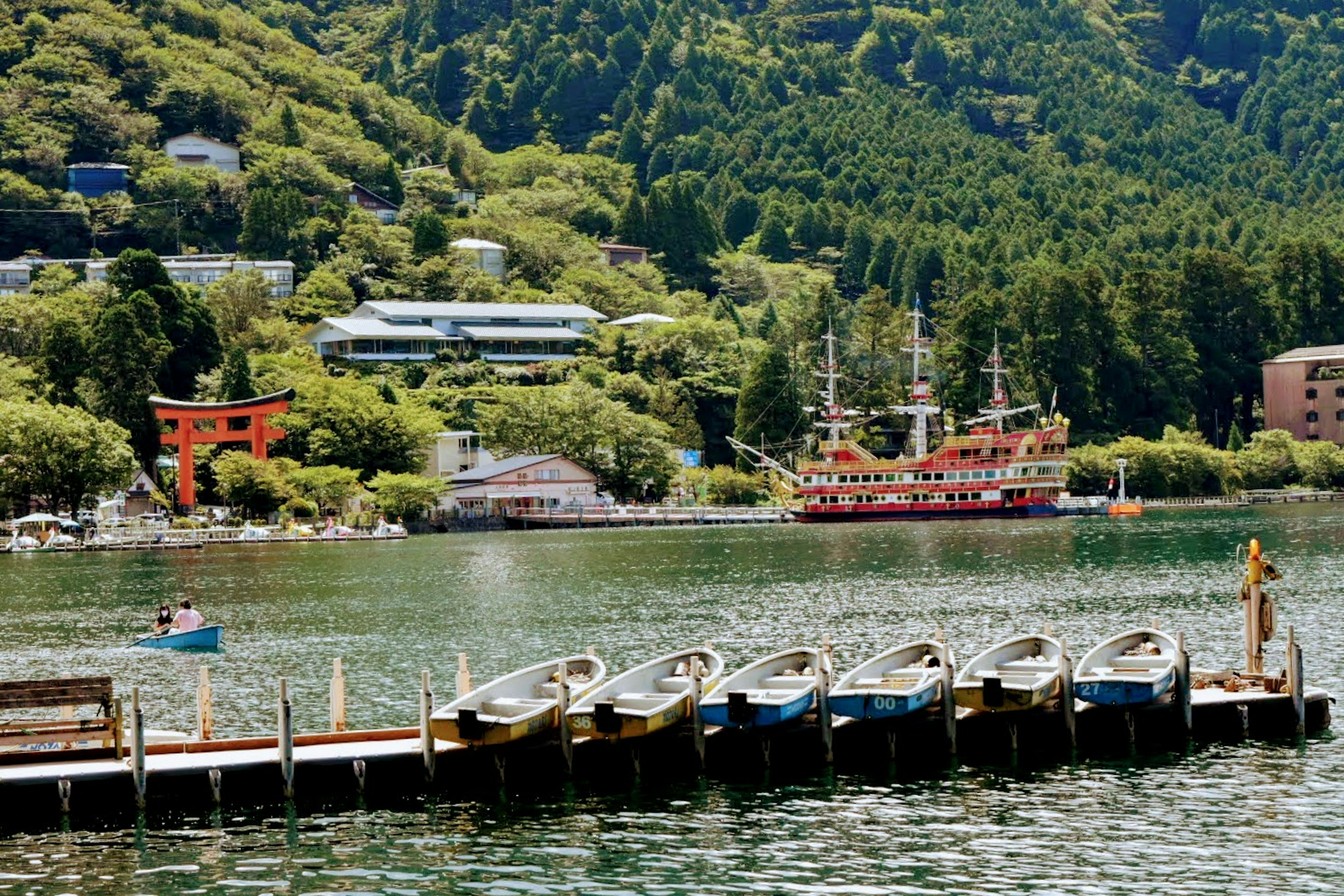 Lakeside dock with boats surrounded by green mountains and a ship in the background