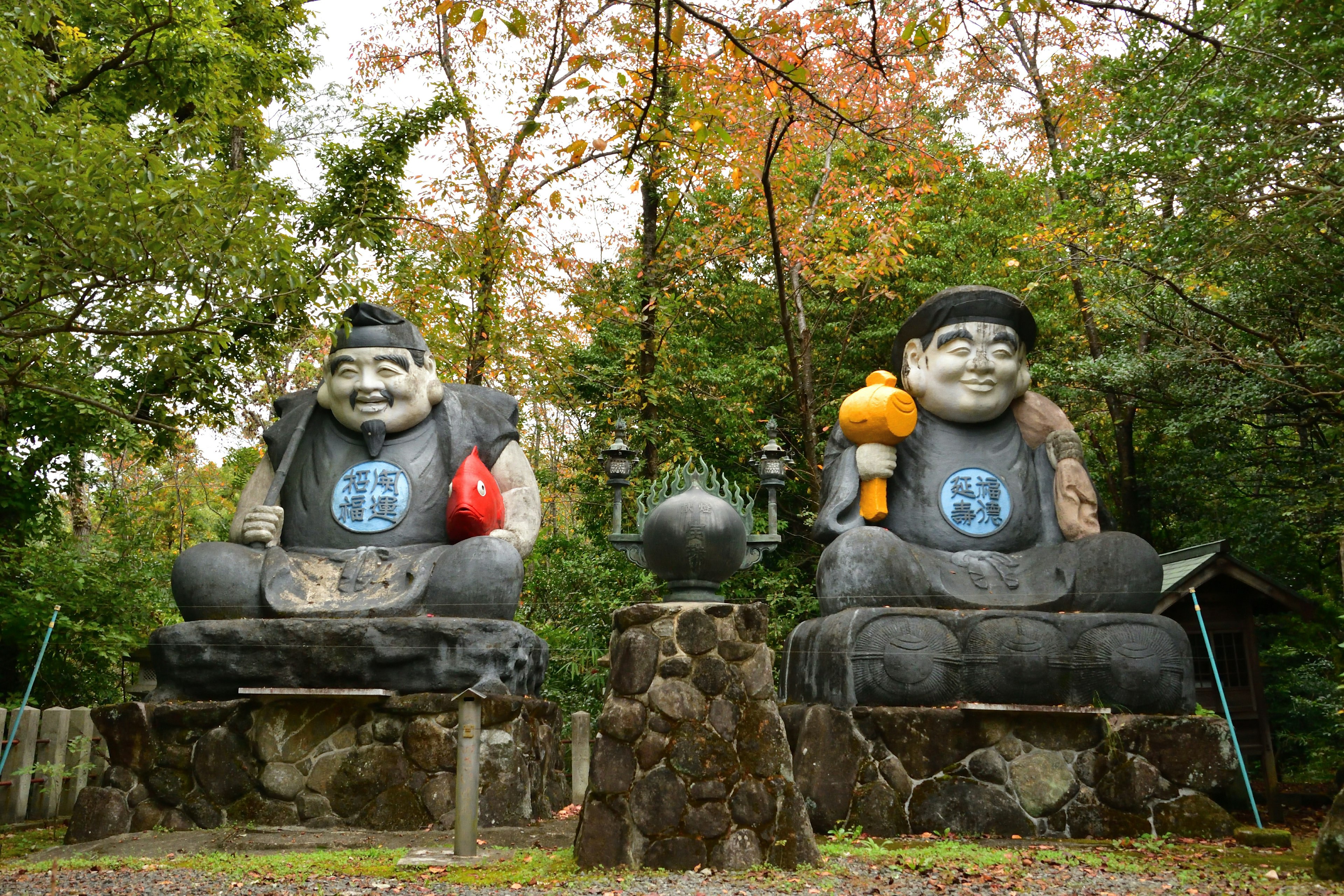 Deux grandes statues de Bouddha assises côte à côte entourées de feuillage d'automne coloré