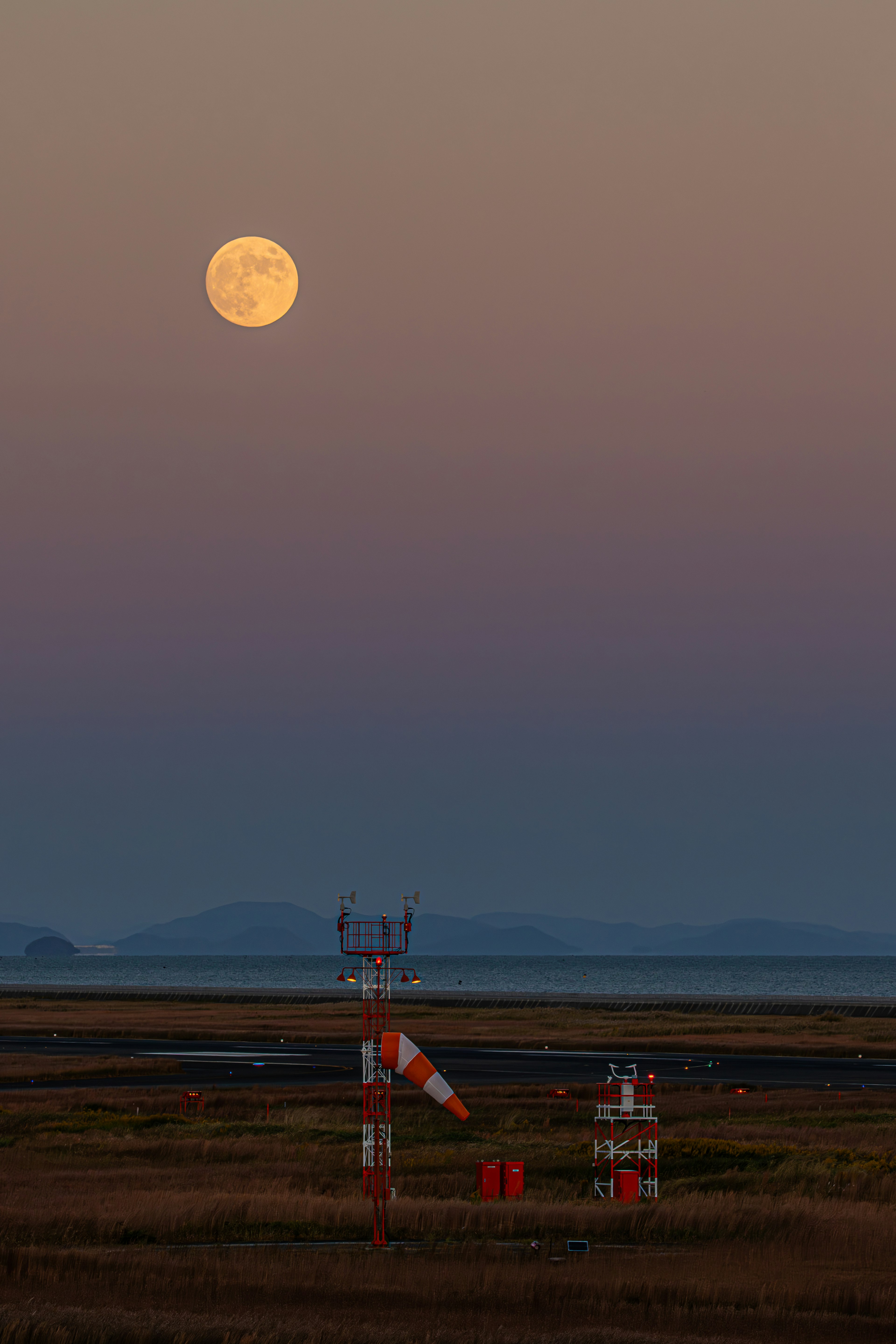 Una luna piena nel cielo serale su un paesaggio con indicatori di direzione del vento e una pista