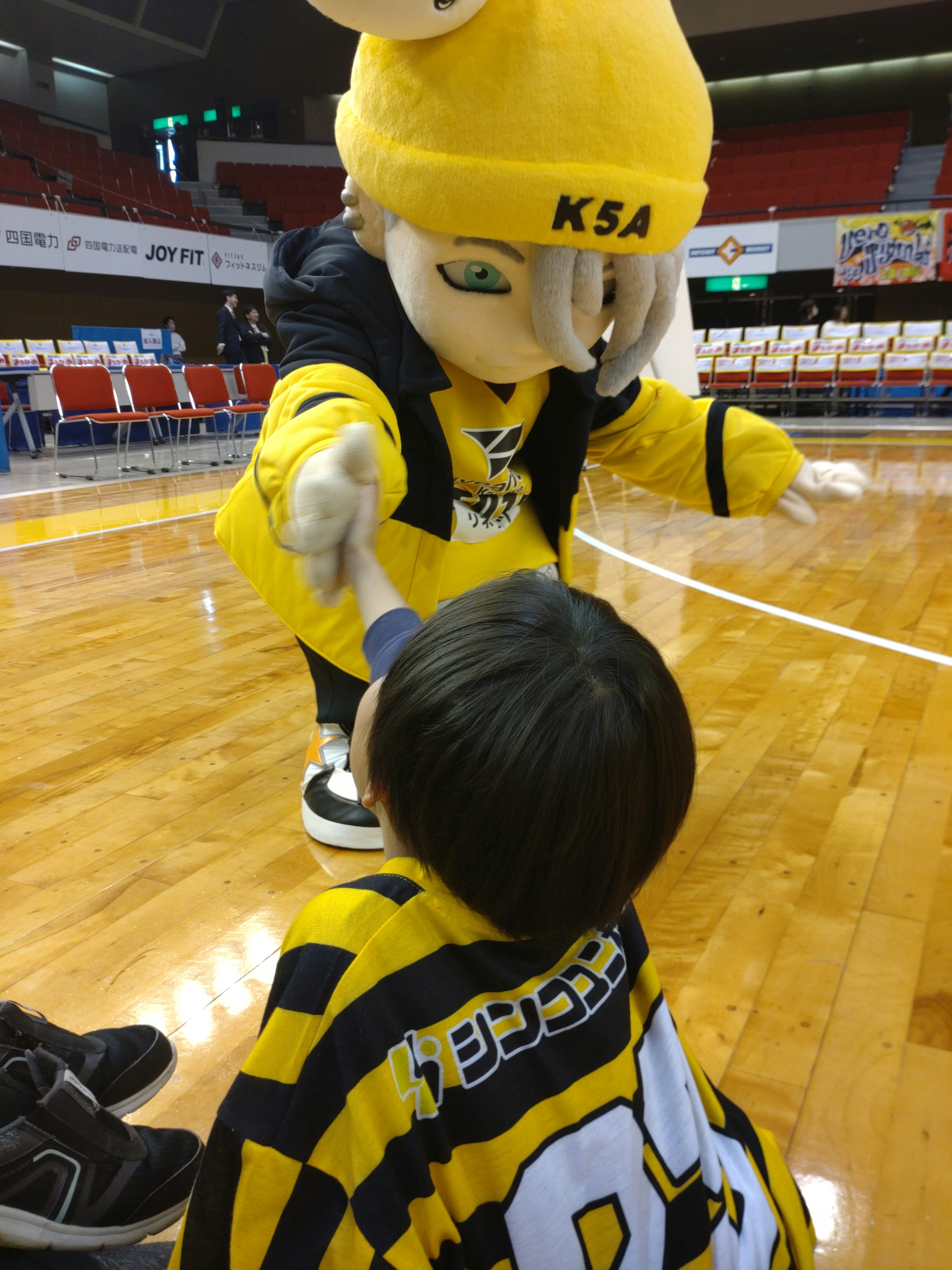 Seorang anak berinteraksi dengan karakter maskot yang mengenakan pakaian kuning dan hitam yang cerah