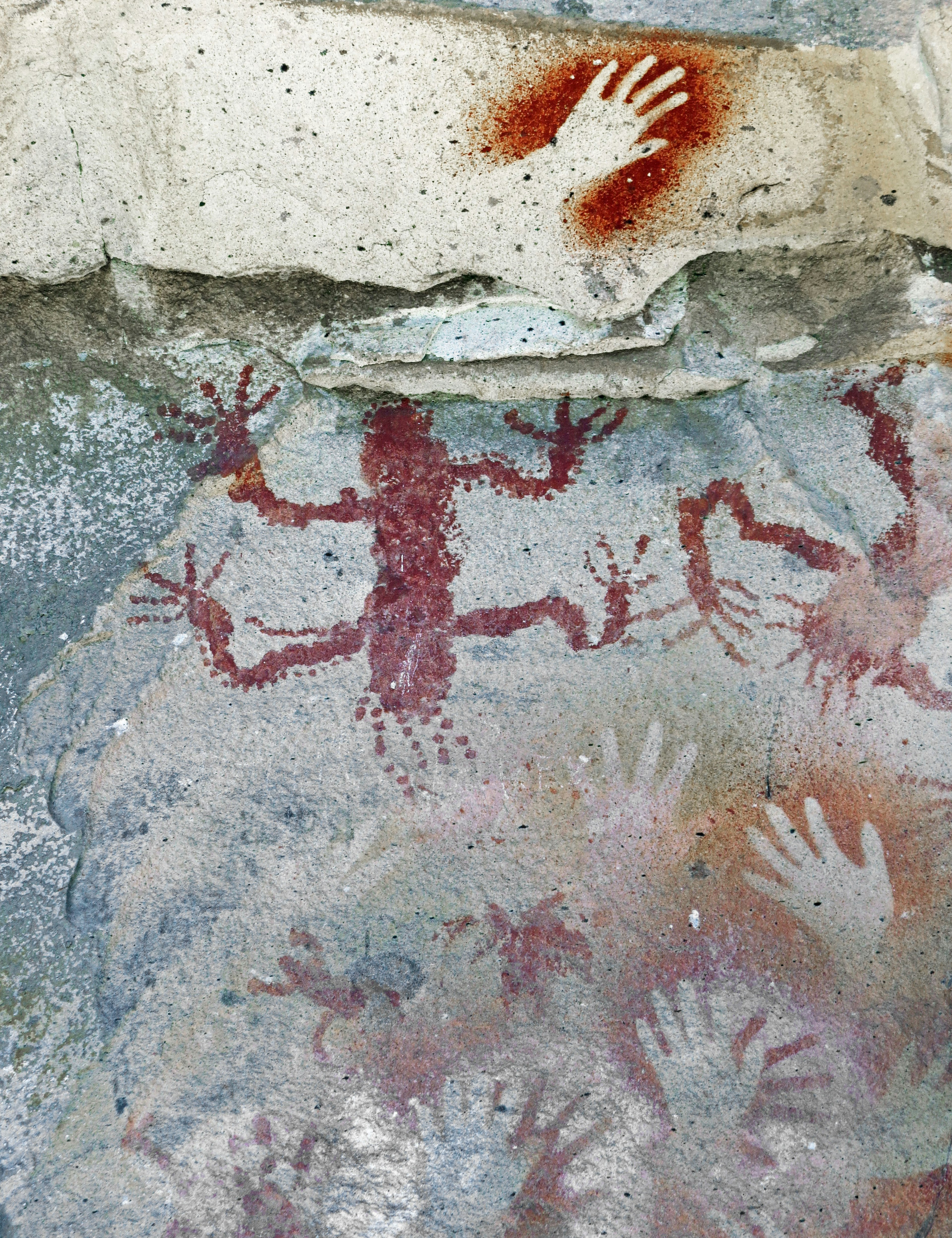 Höhlenwand mit roten Handabdrücken und Reptilzeichnungen