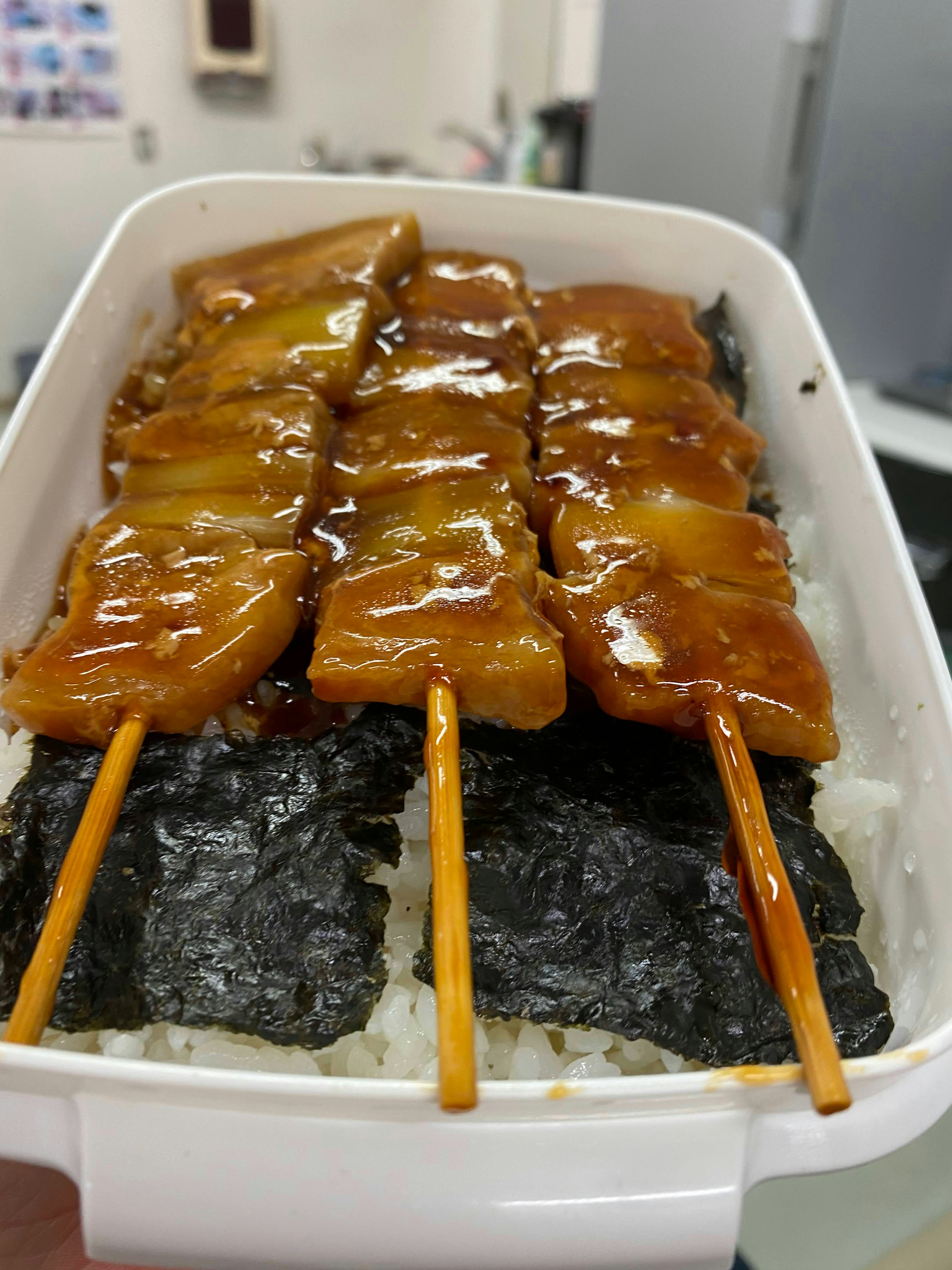 Hidangan dengan tusuk sate panggang dengan saus teriyaki di atas nasi dan rumput laut