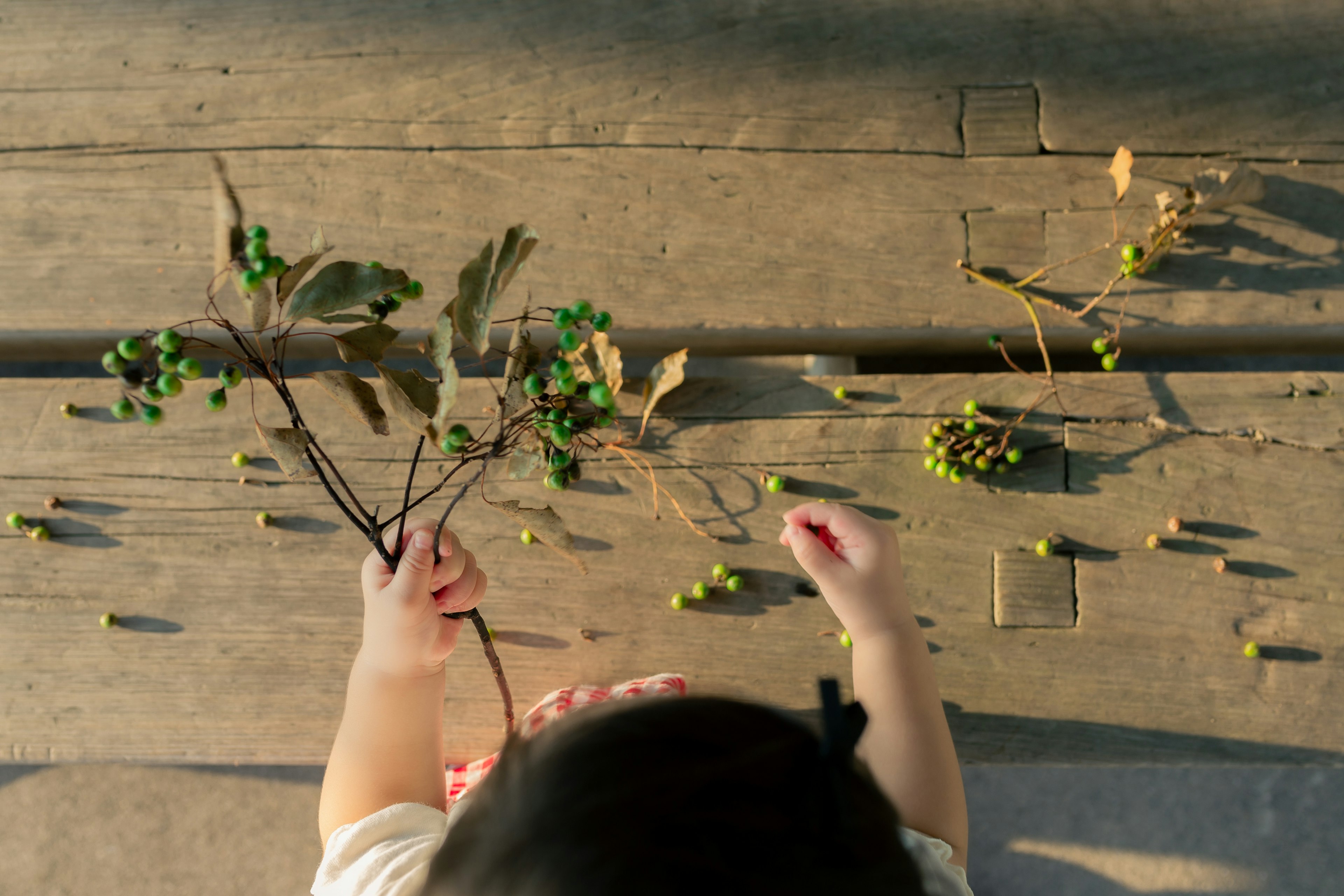 Kind spielt mit Zweigen und grünen Beeren auf einer Holzoberfläche