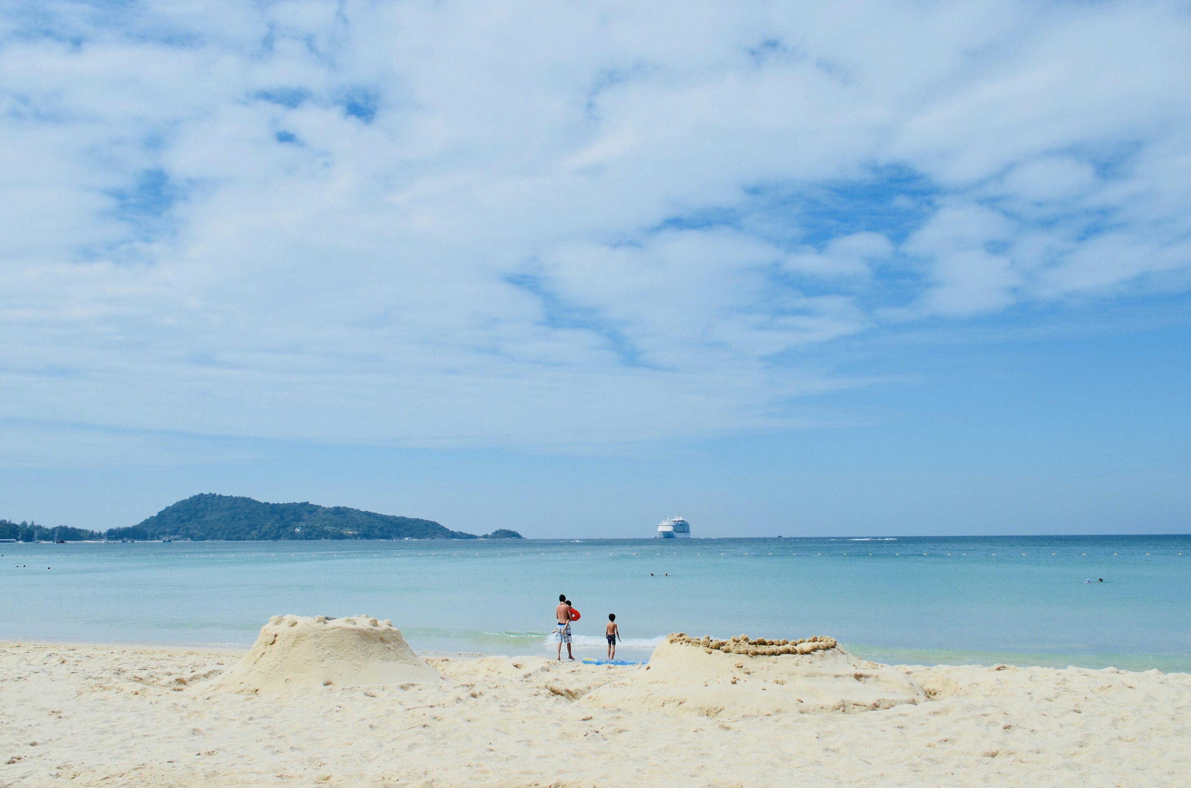 Niños jugando cerca de castillos de arena en una playa con mar y cielo azul