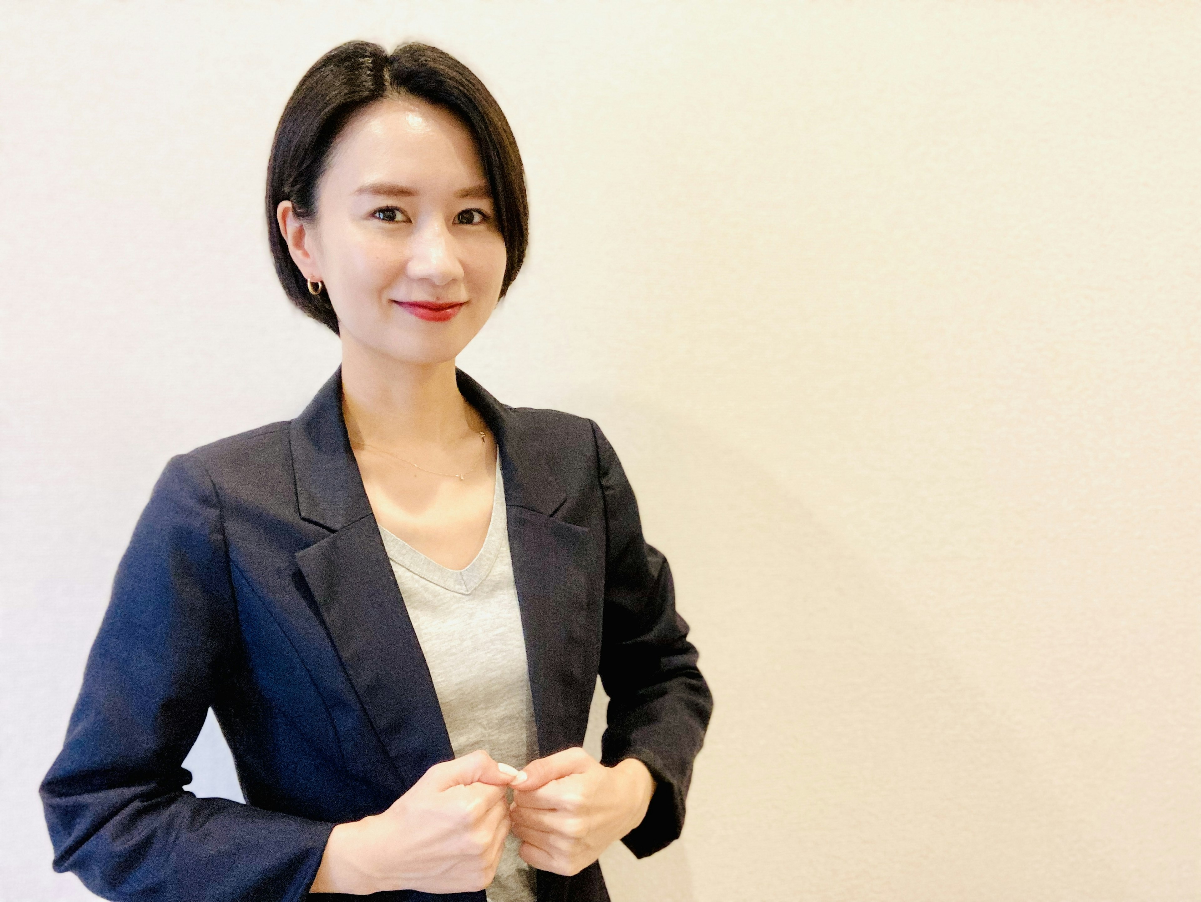 A woman in a suit smiling in front of a simple background