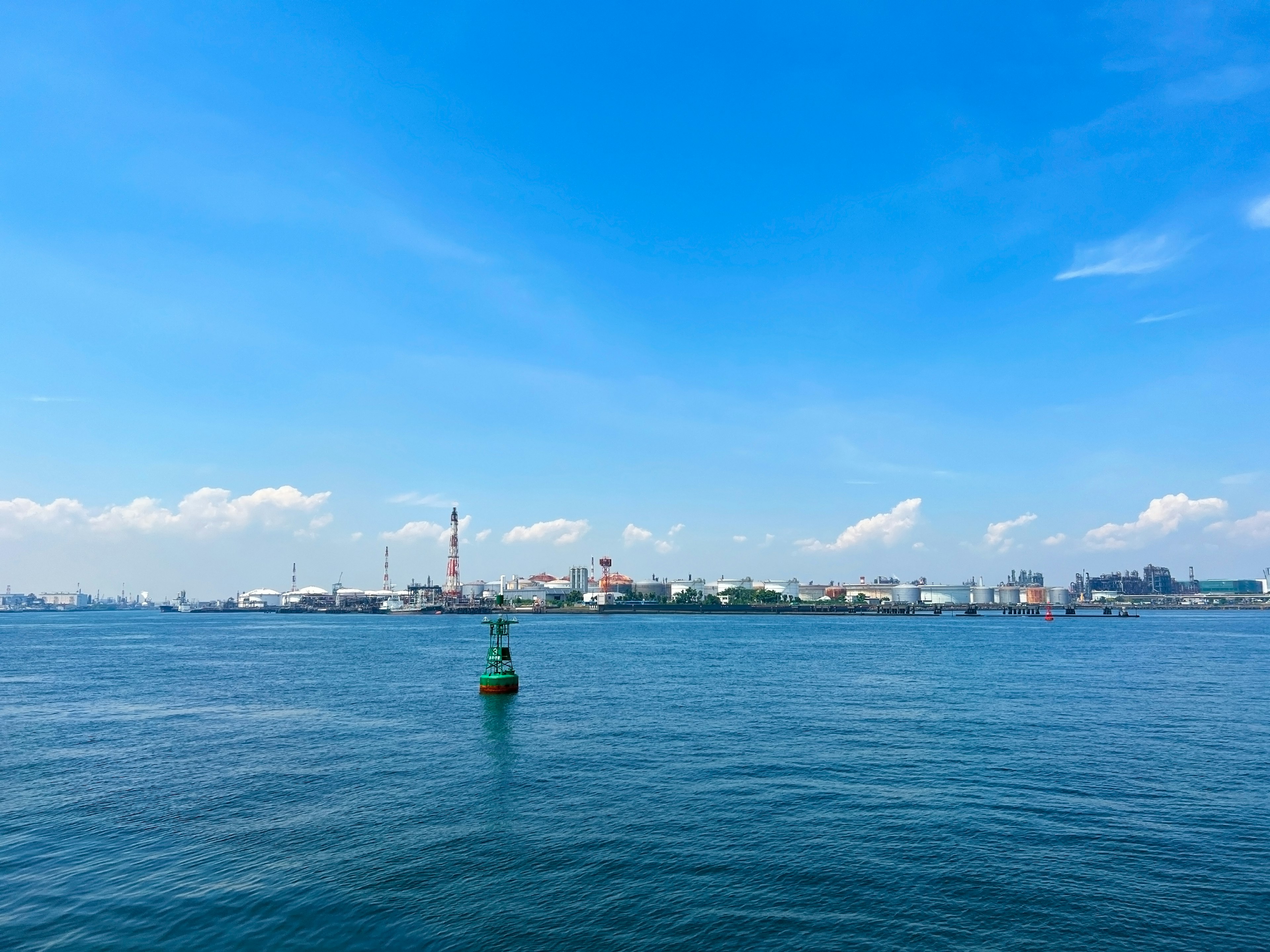 Scène maritime sous un ciel bleu avec une bouée verte flottant sur l'eau