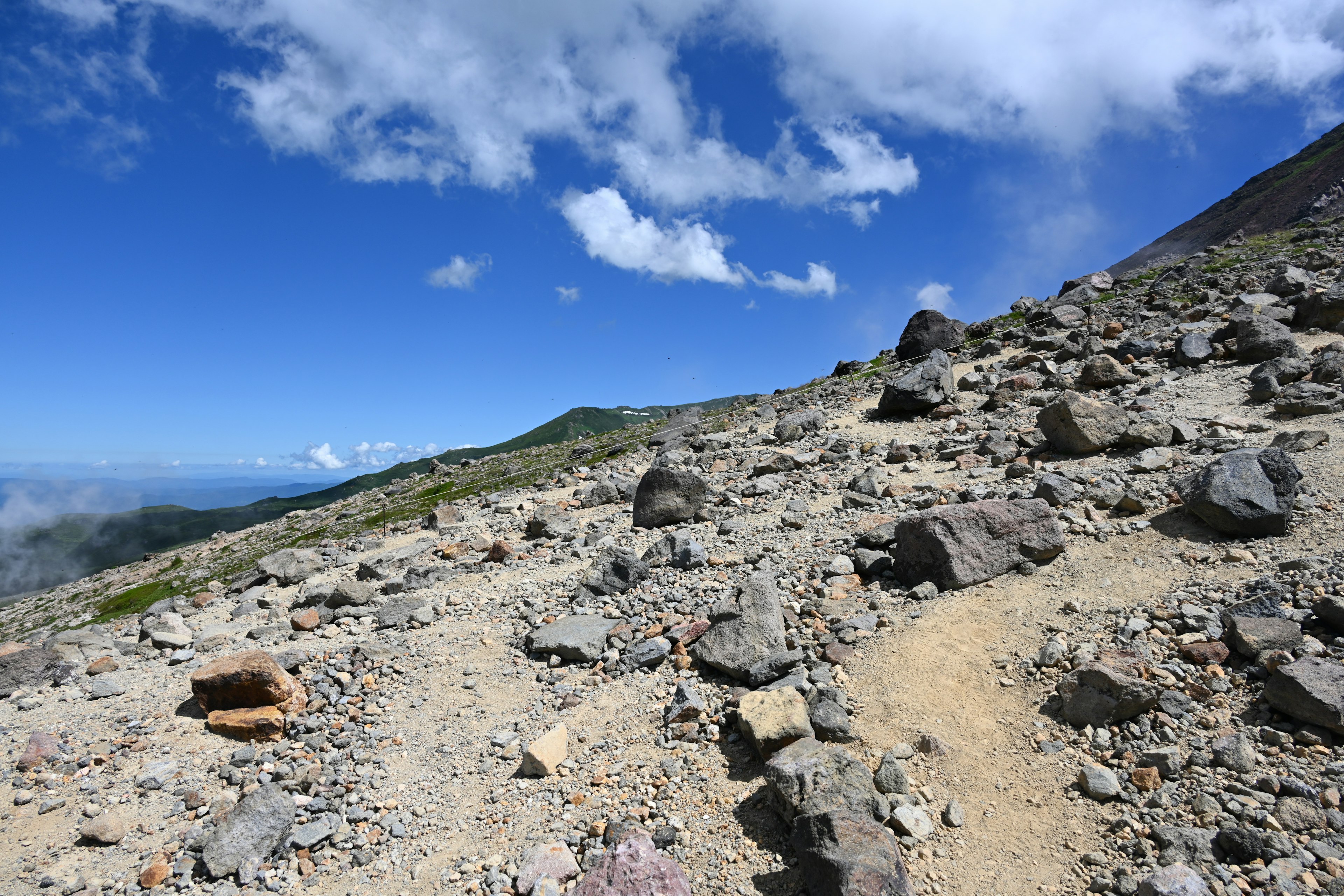 Rocky trail on a mountain slope with bright blue sky and white clouds