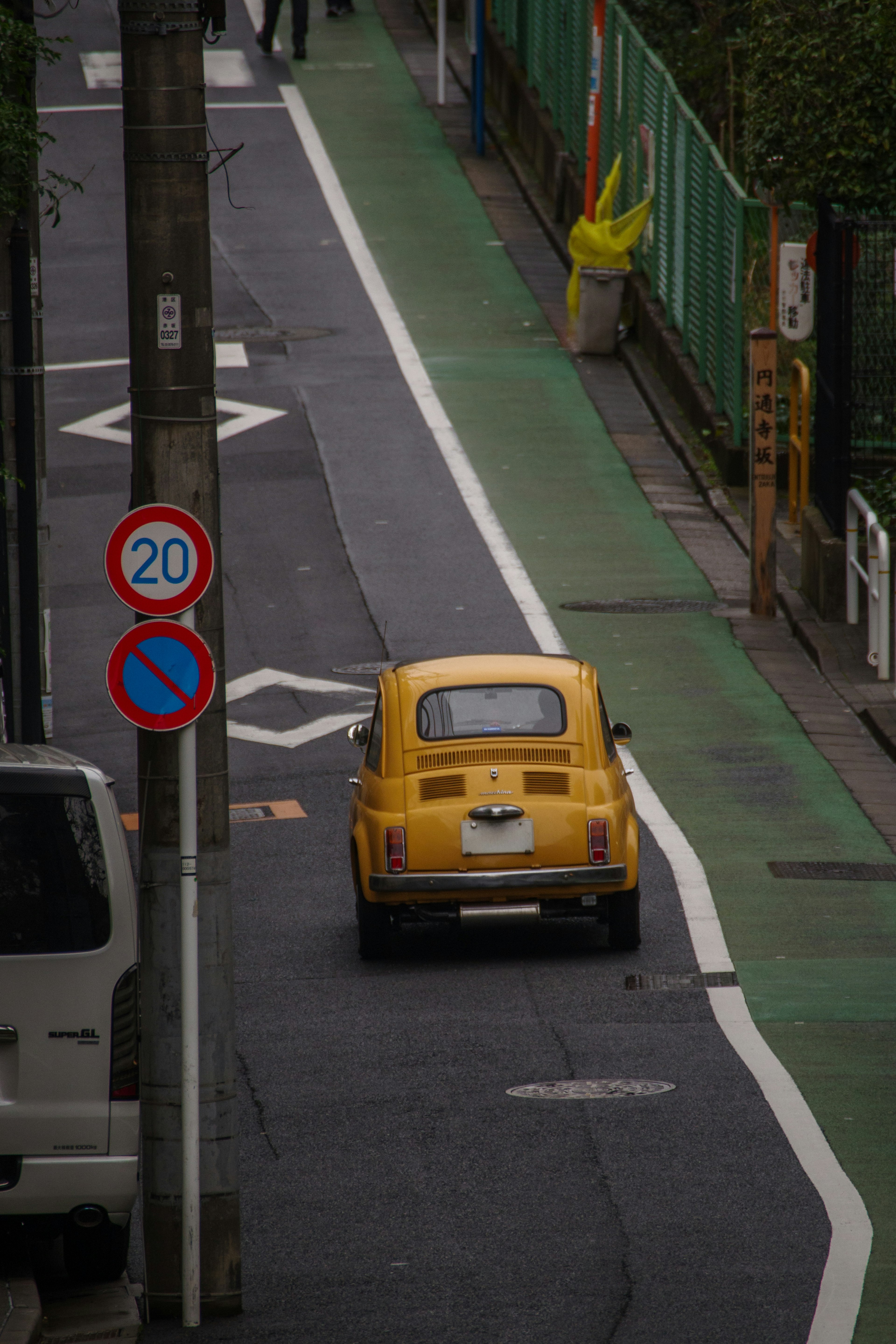 A small yellow car driving on a narrow street