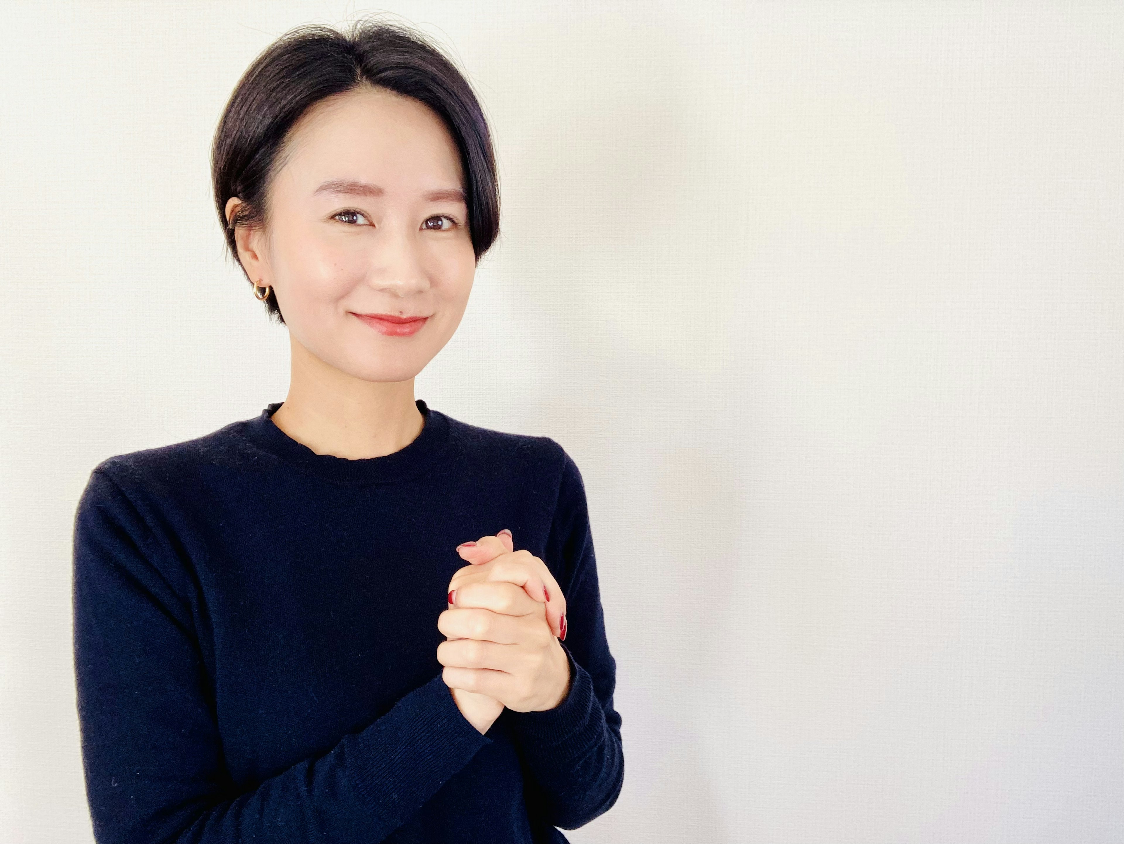 Une femme souriante avec les mains jointes devant un fond blanc