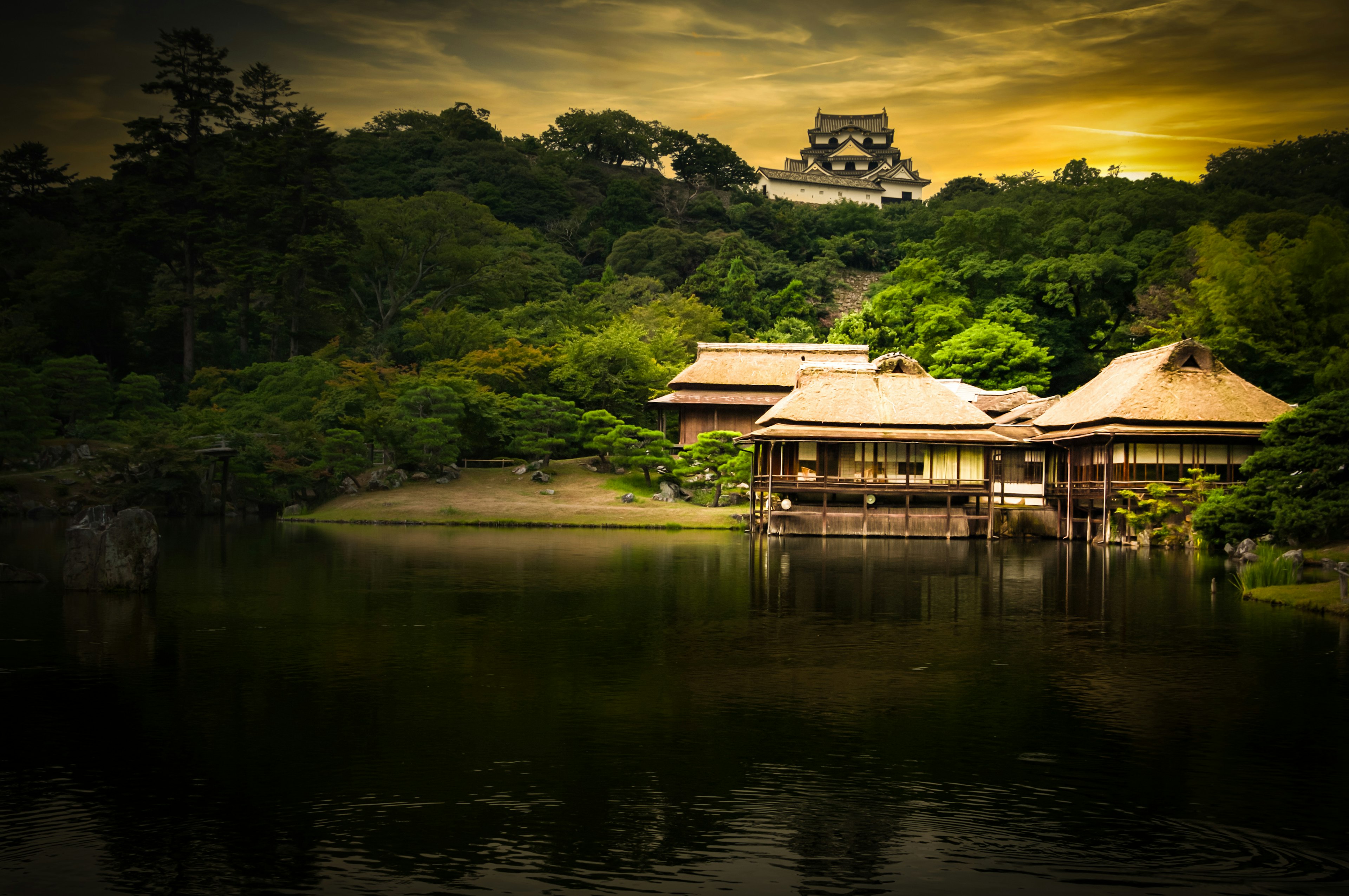 Traditionelle japanische Häuser am ruhigen Teich, der den Sonnenuntergang widerspiegelt und von üppigem Grün umgeben ist