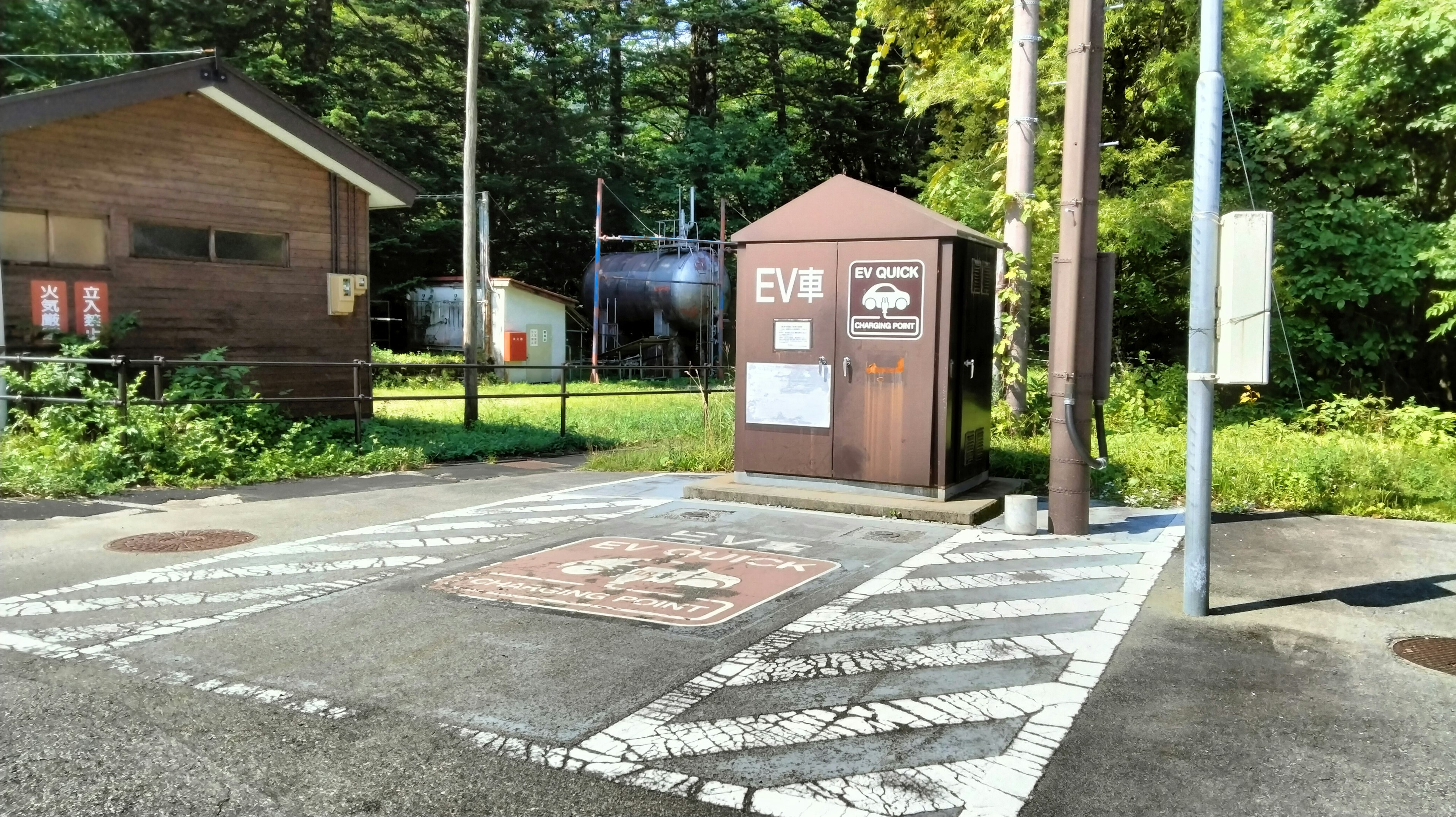 緑に囲まれた木造の小屋とEV充電ステーションがある風景