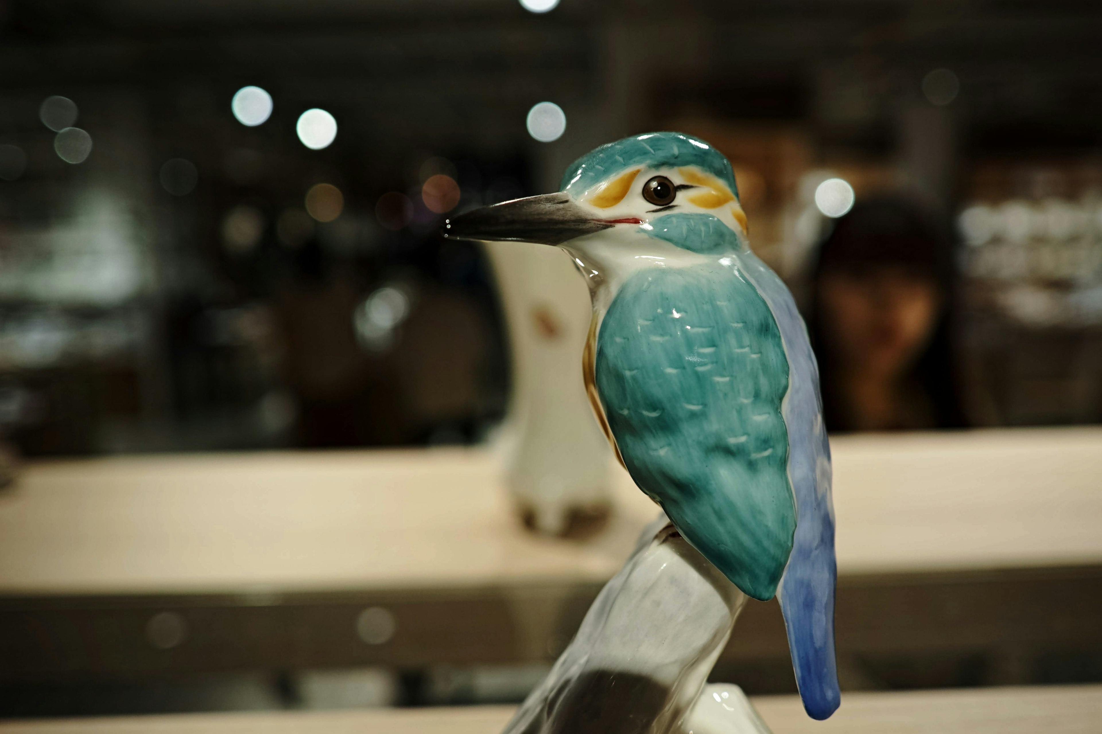 Figurita de cerámica de un pájaro azul con un fondo borroso de una persona