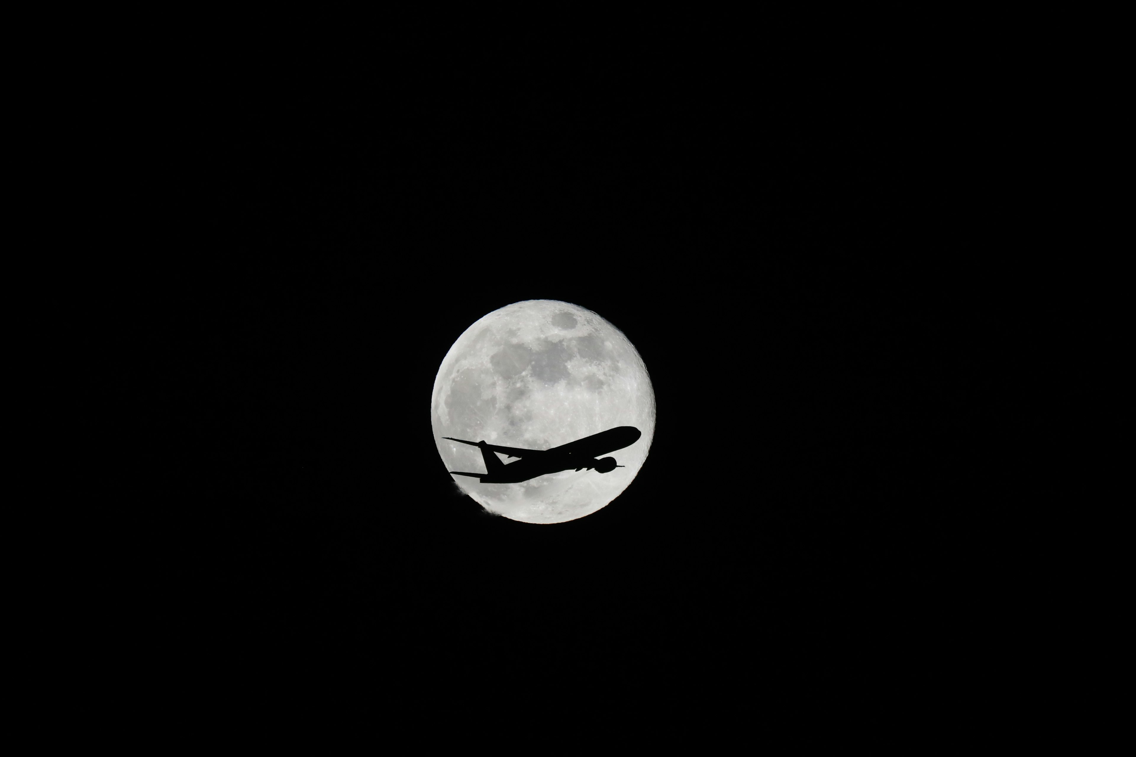 Silhouette di un aereo che vola davanti alla luna