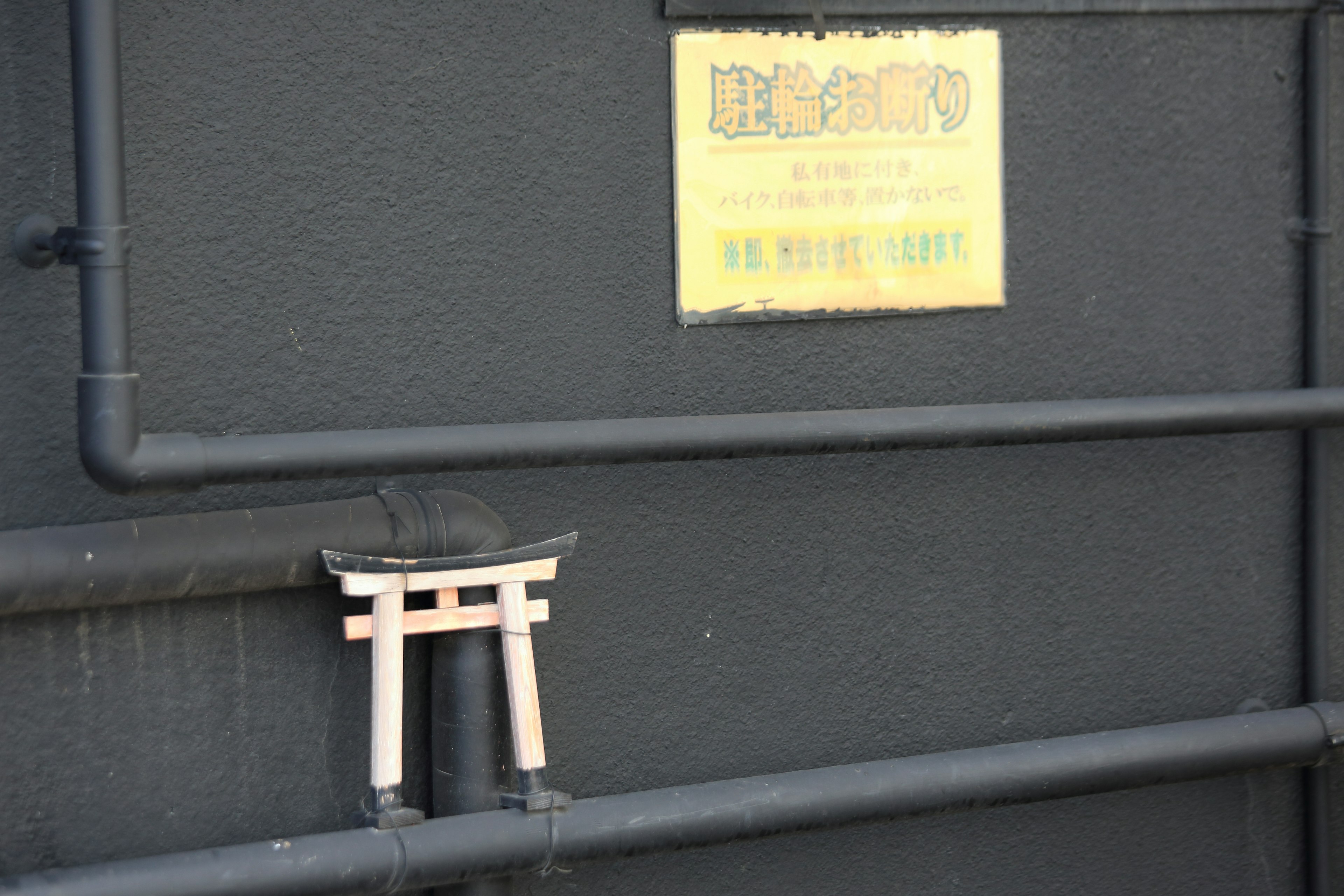 Small wooden torii gate mounted on a black wall with a yellow sign