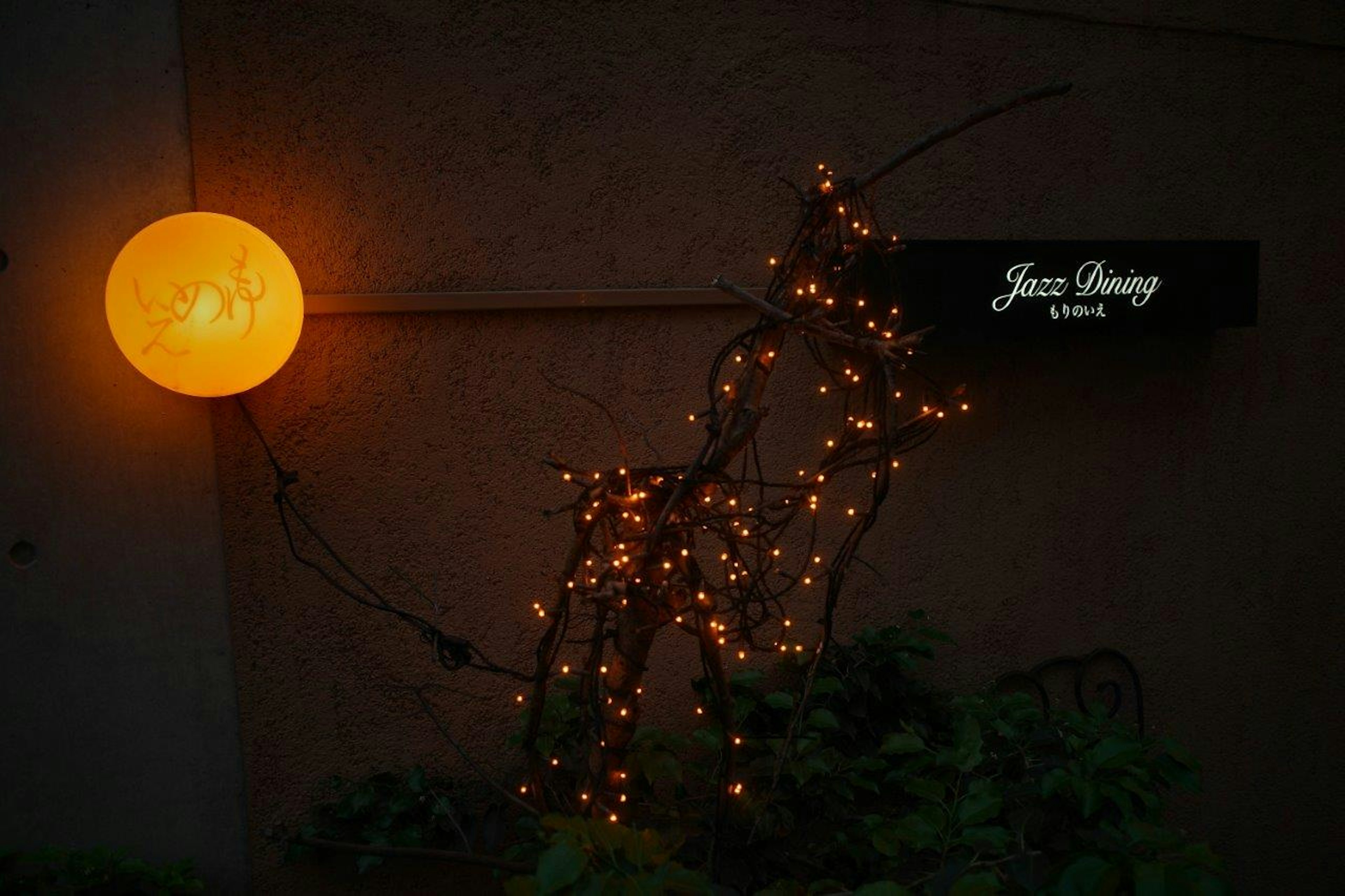 Luz esférica naranja al lado de una escultura de ciervo iluminada hecha de ramas y un letrero de Jazz Dining