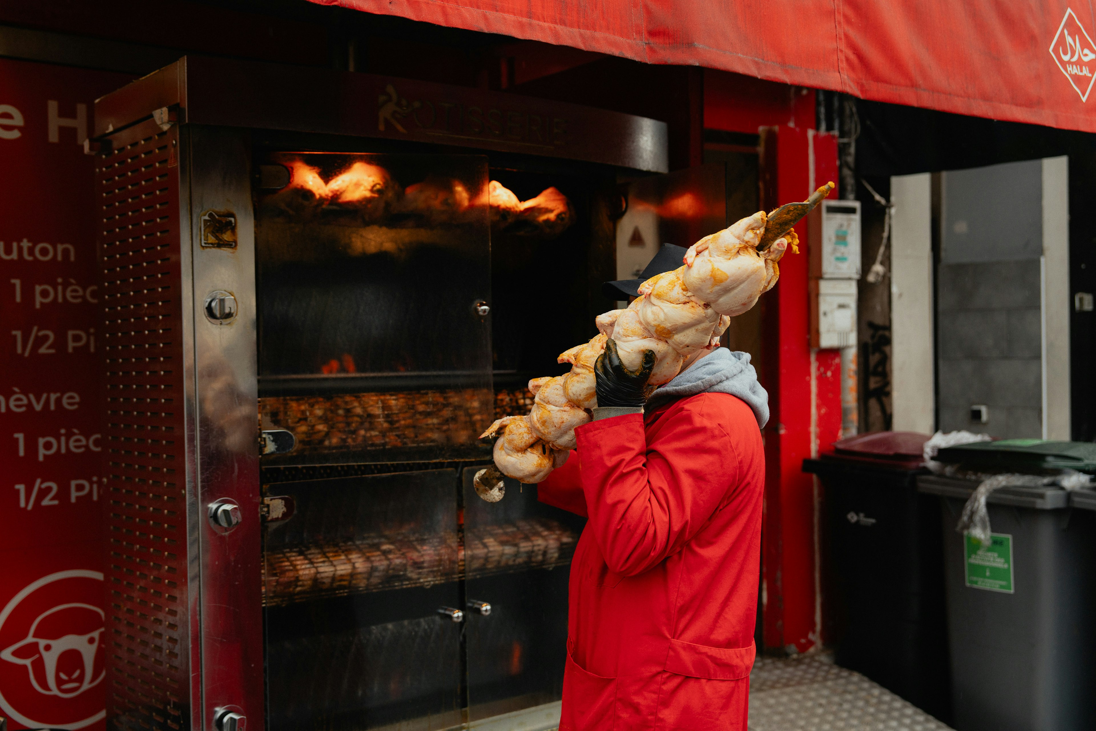 Persona con abrigo rojo sosteniendo comida en brochetas frente a un asador