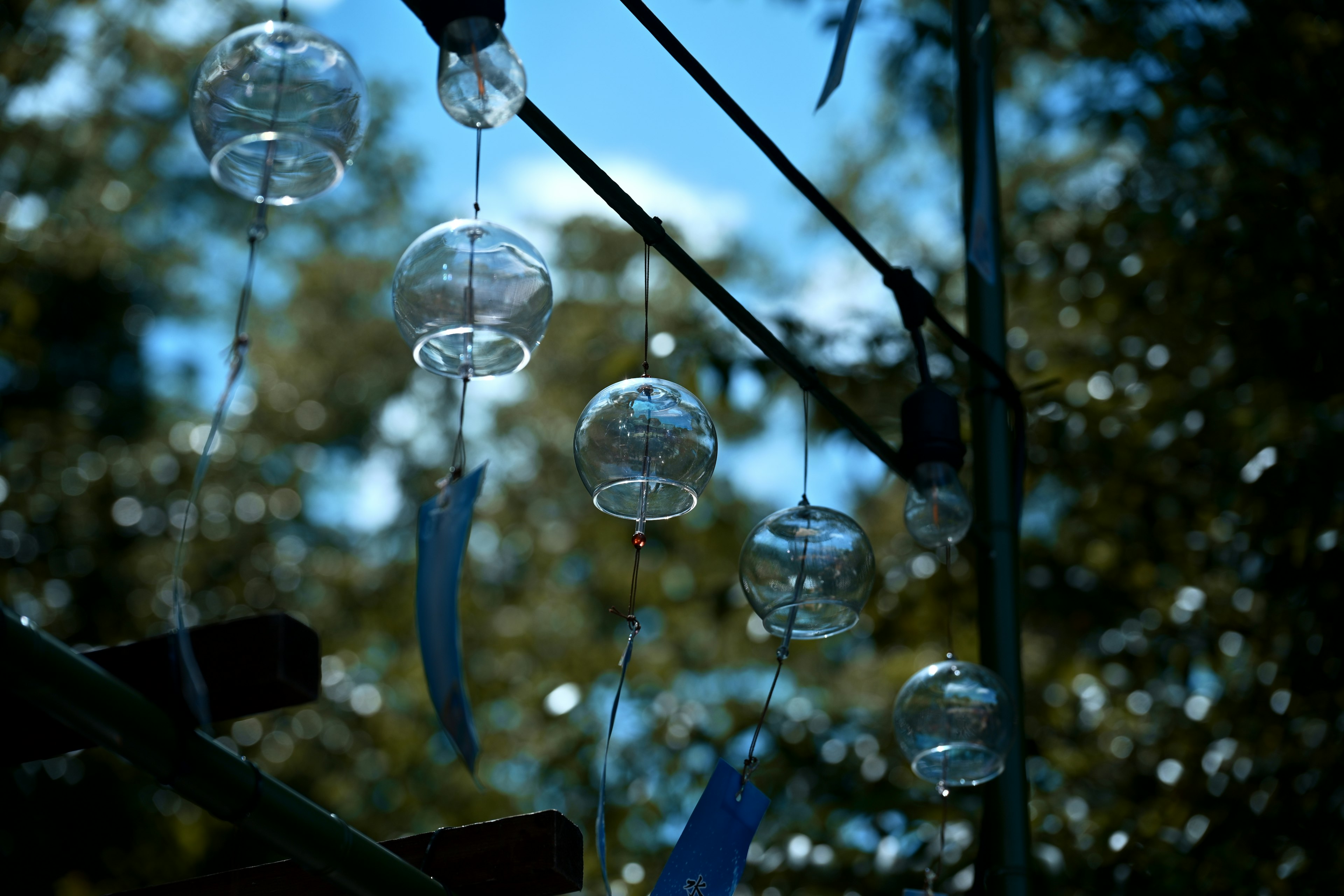 Wind chimes swaying under a blue sky featuring clear glass and blue ribbons