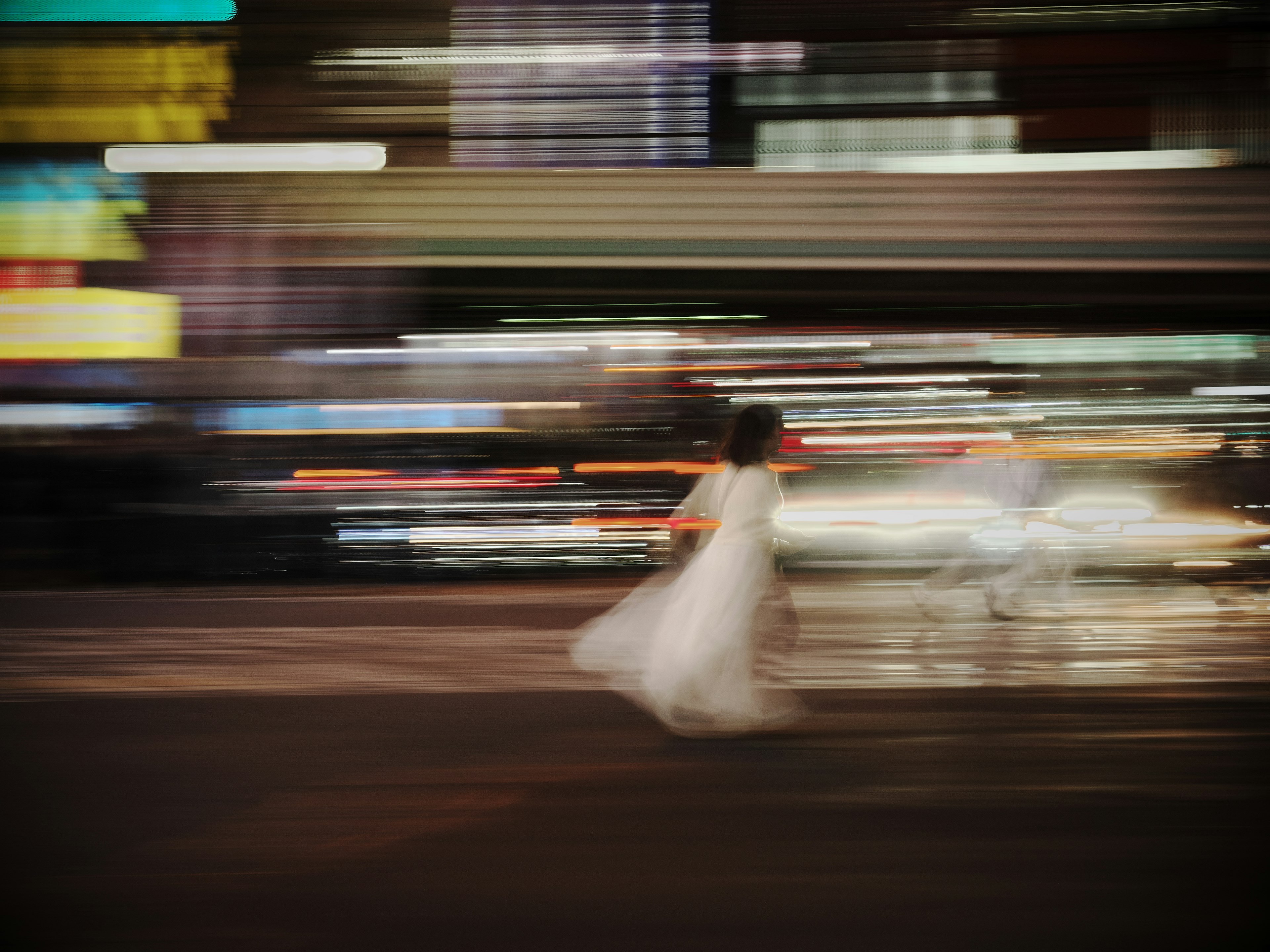 A blurred photo of a woman in a white dress rushing across a city street