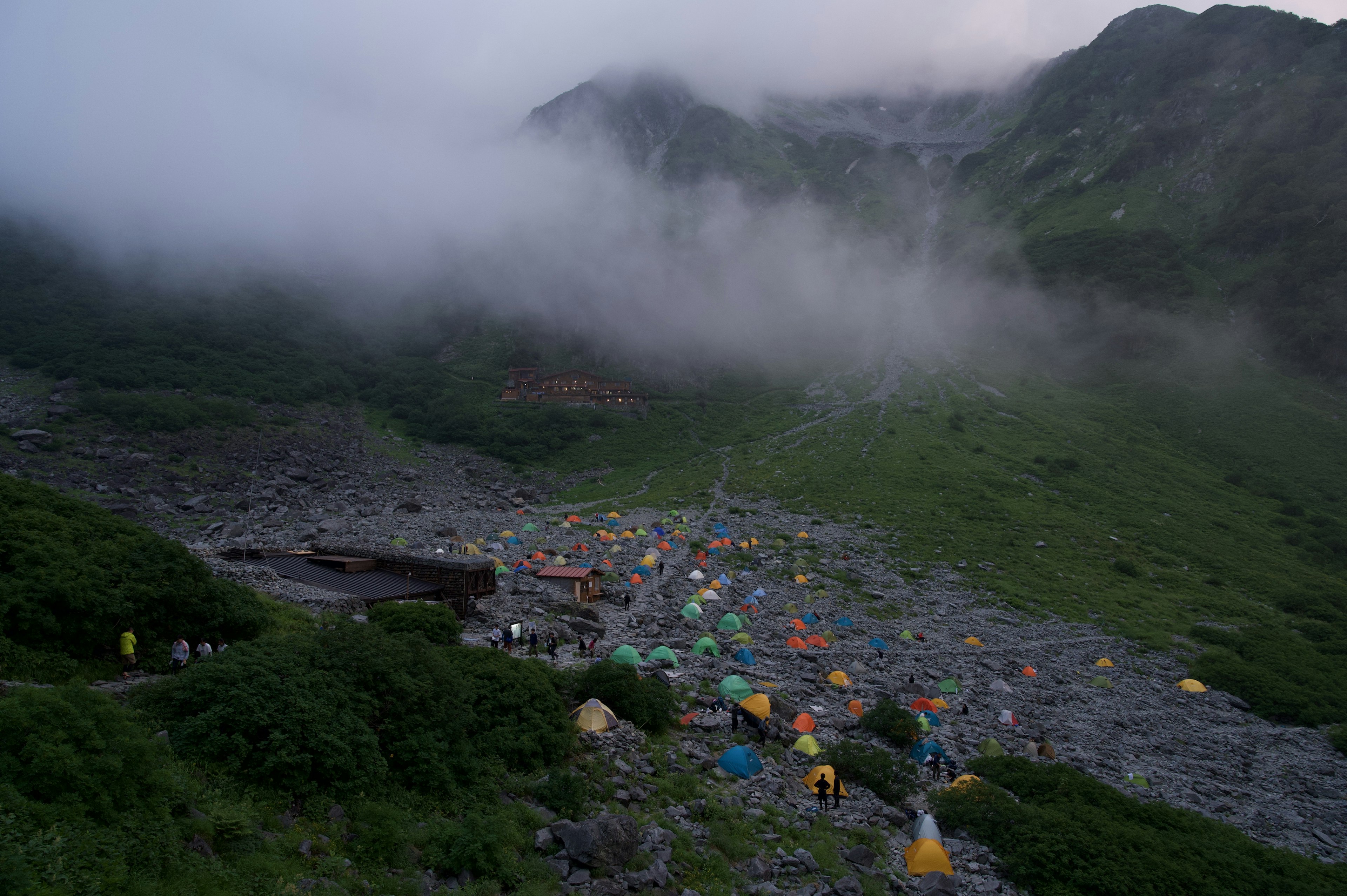 Vue d'un camp coloré avec des tentes dispersées sur un paysage rocheux en montagne