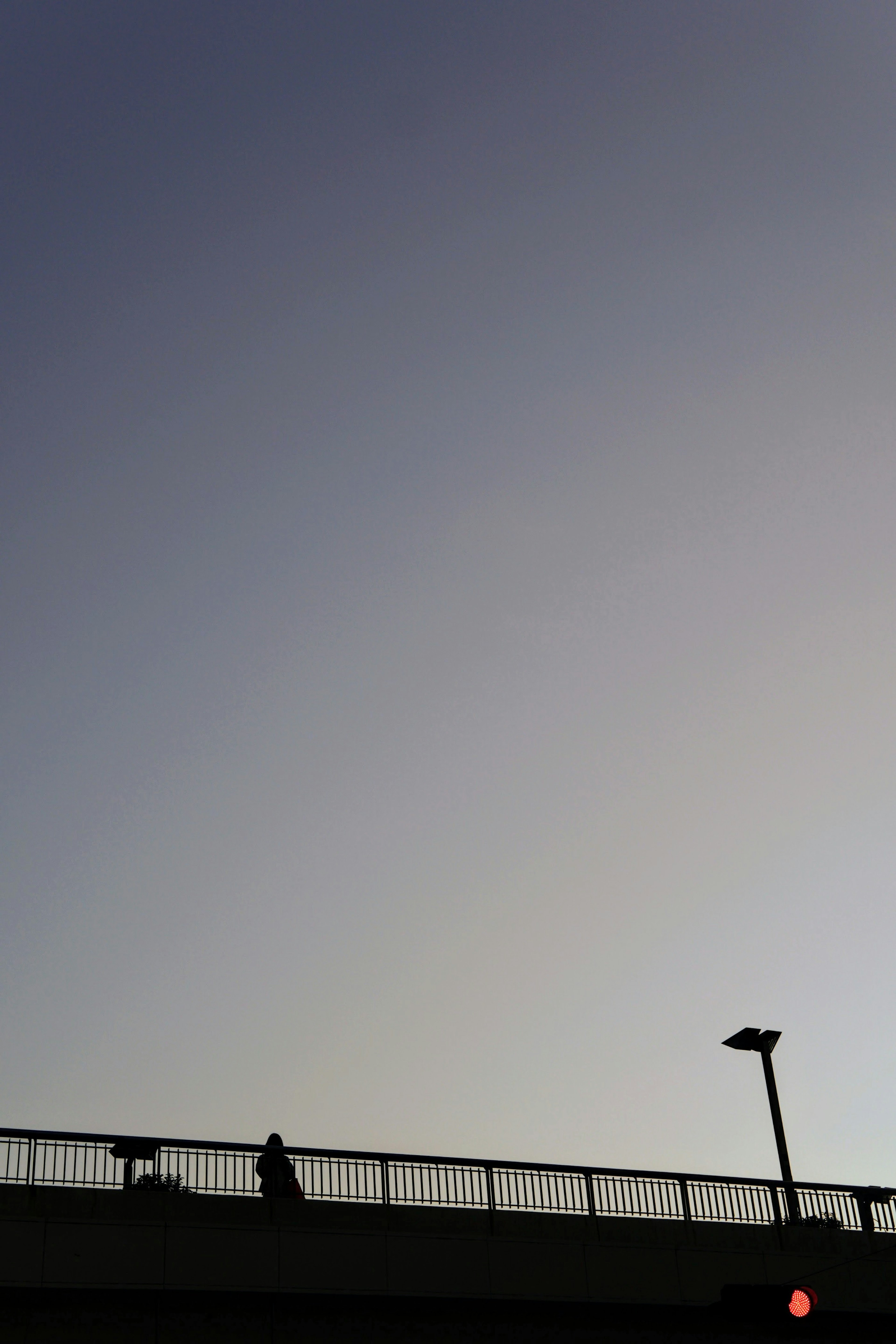 Silhouette of a person on a bridge against a blue sky