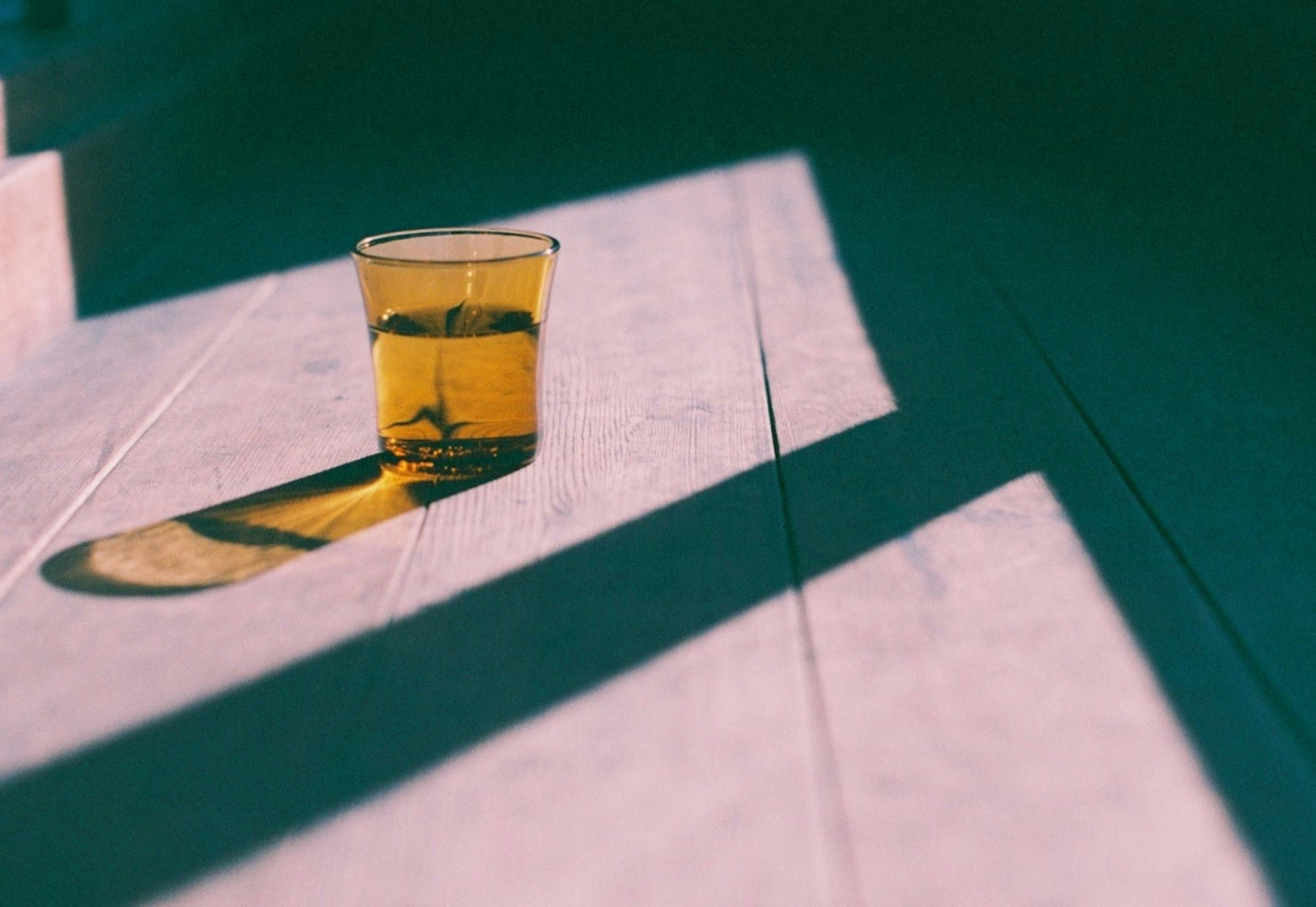 Ein transparentes Glas mit gelbem Getränk auf dem Boden, das Schatten wirft