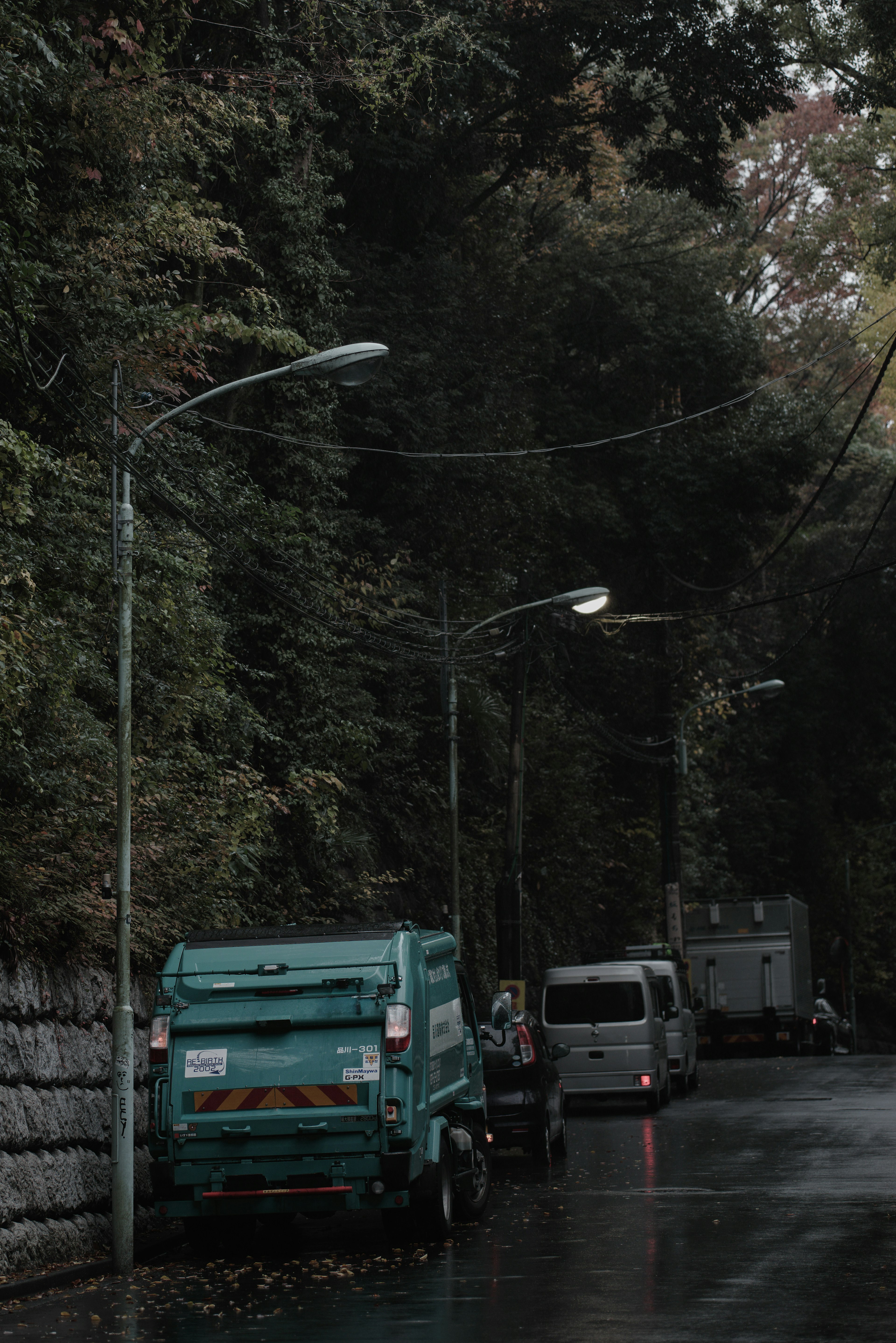 Escena de calle tranquila con un camión de basura verde y farolas