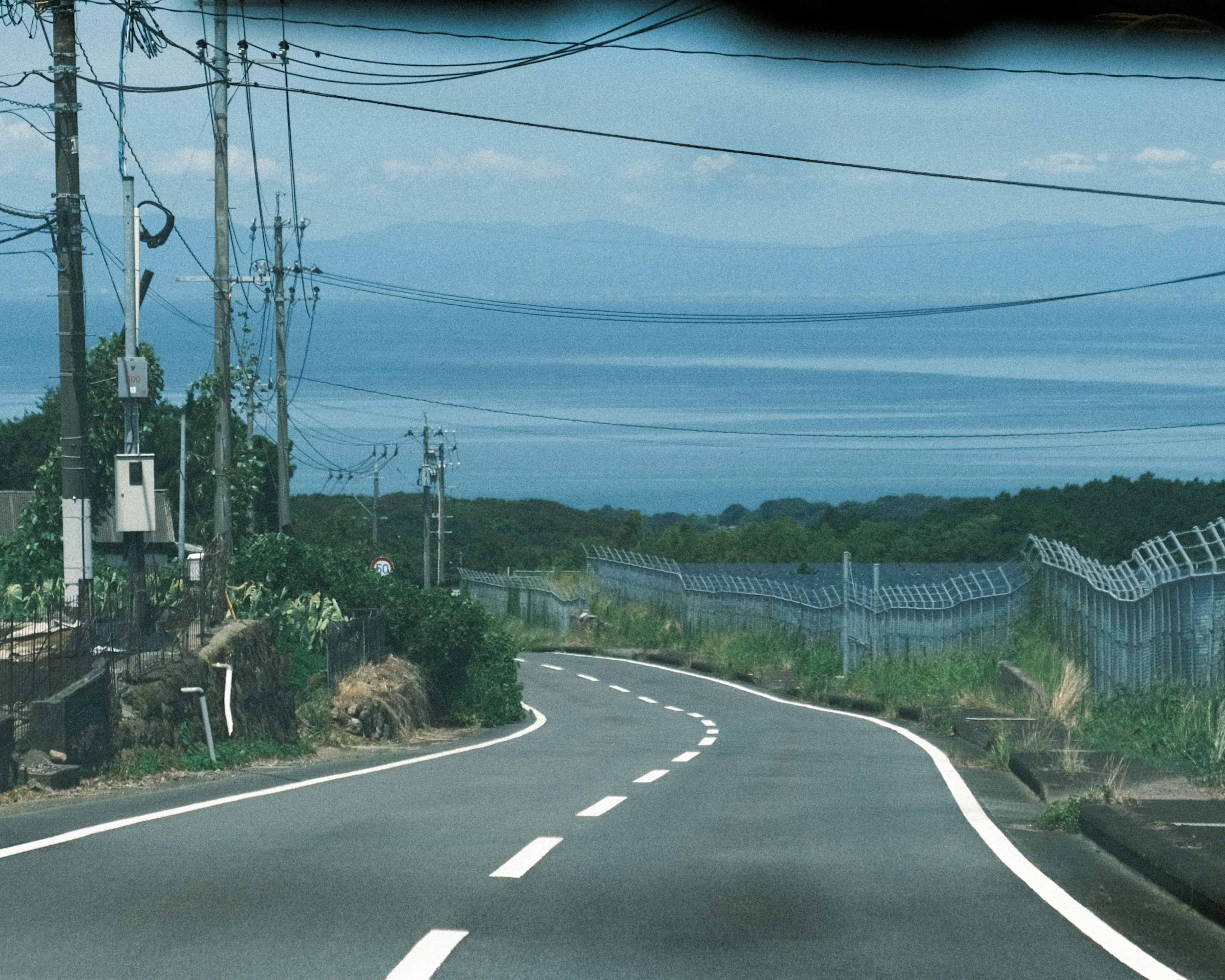 Kurvenreiche Straße mit blauem Meer und Himmel im Hintergrund