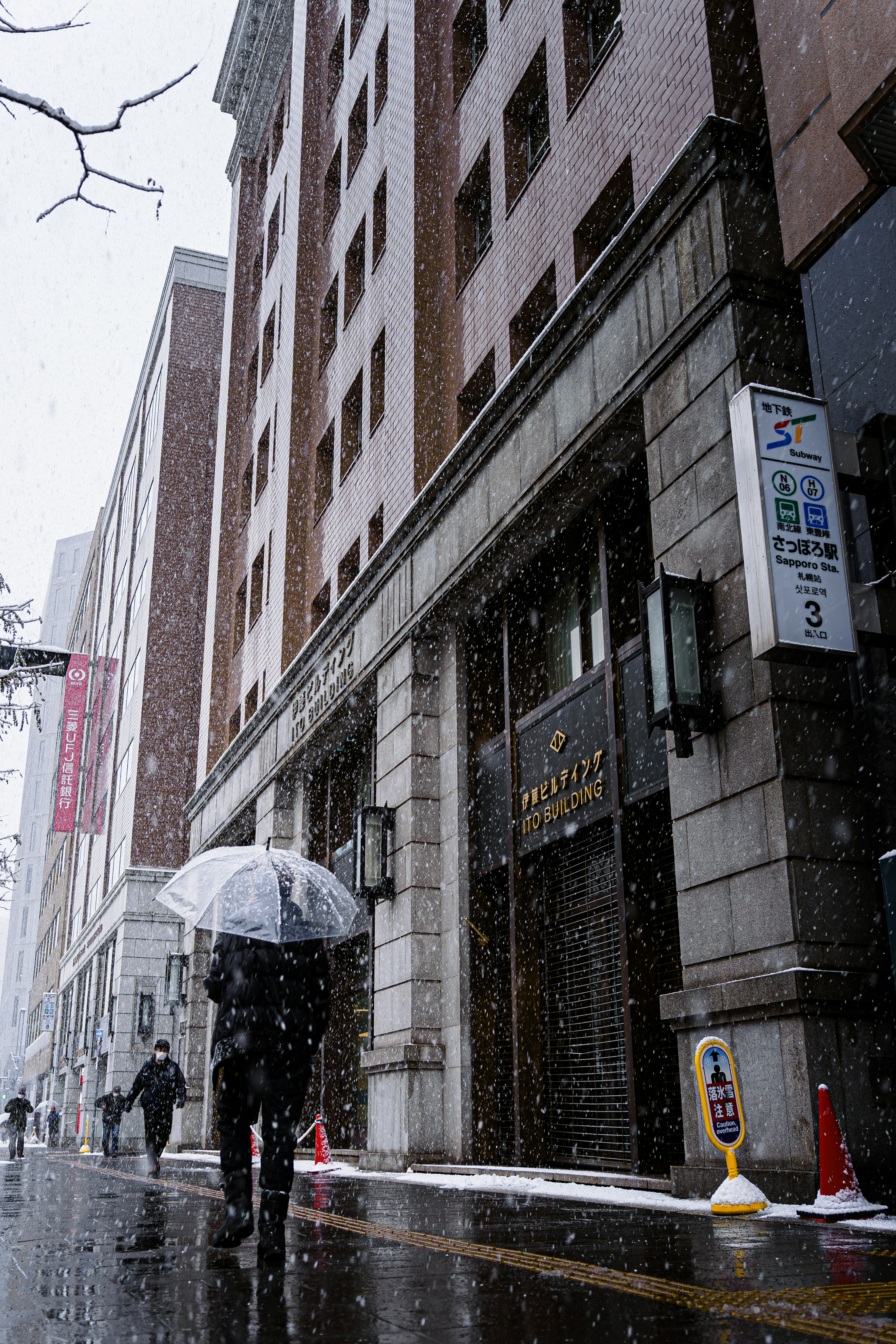 雪の降る街中を傘をさして歩く人と高層ビルの風景