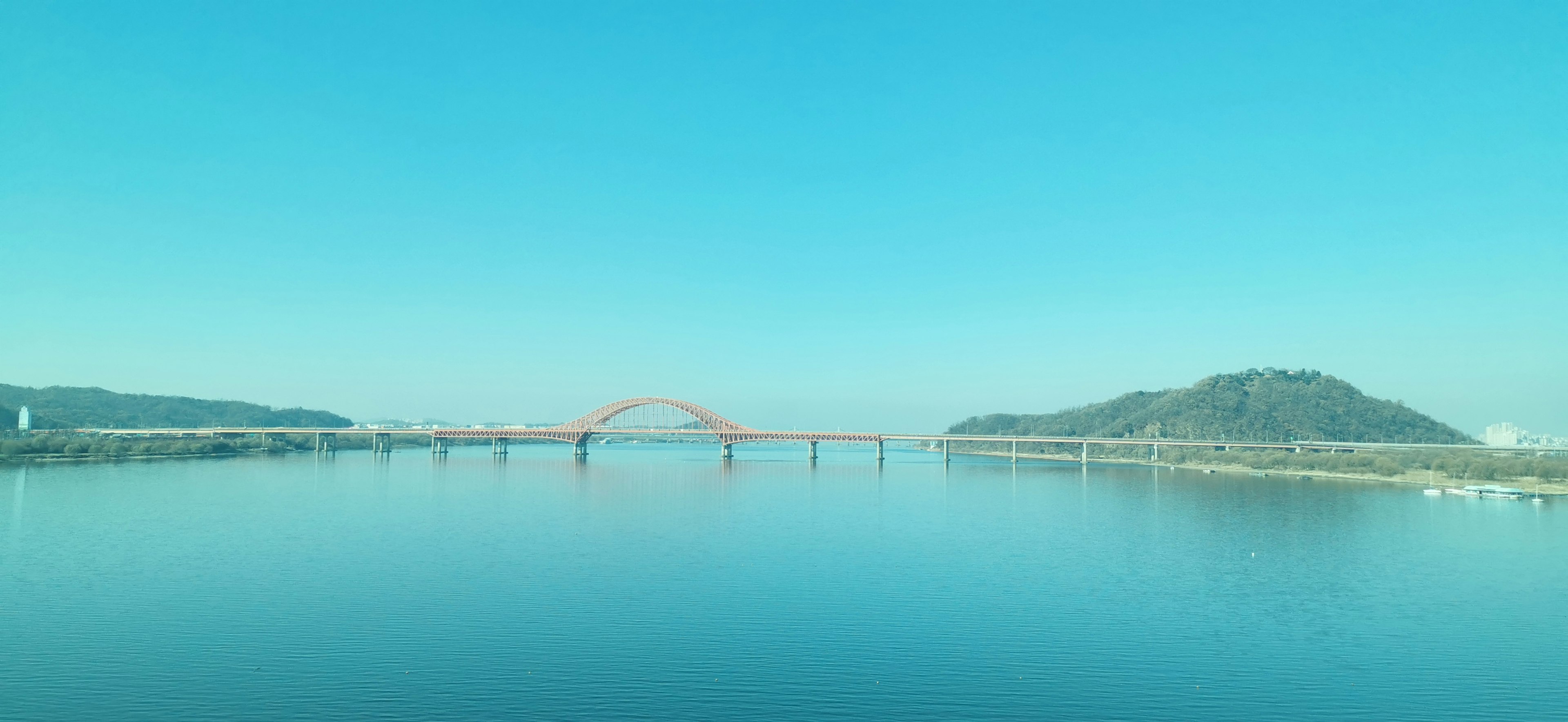 Vista escénica de un puente rojo sobre aguas tranquilas con montañas al fondo