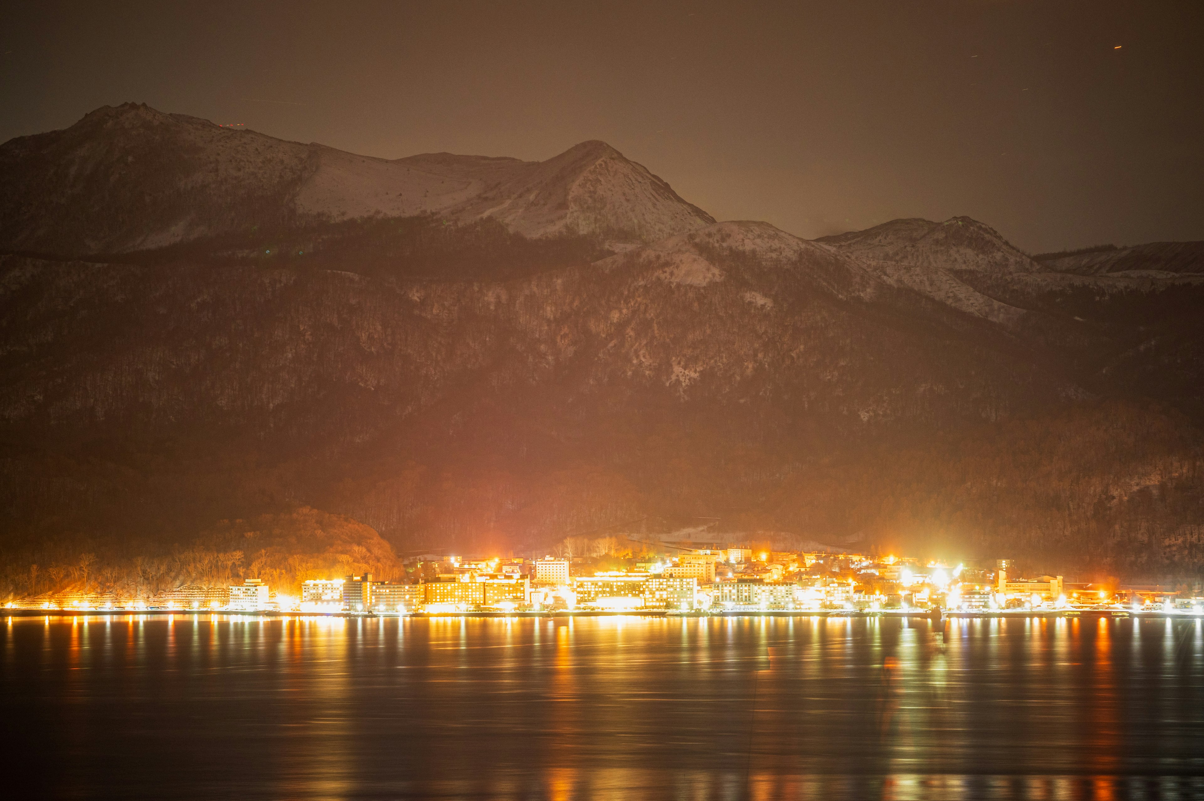 雪の山々を背景にした夜の湖畔の町の灯り