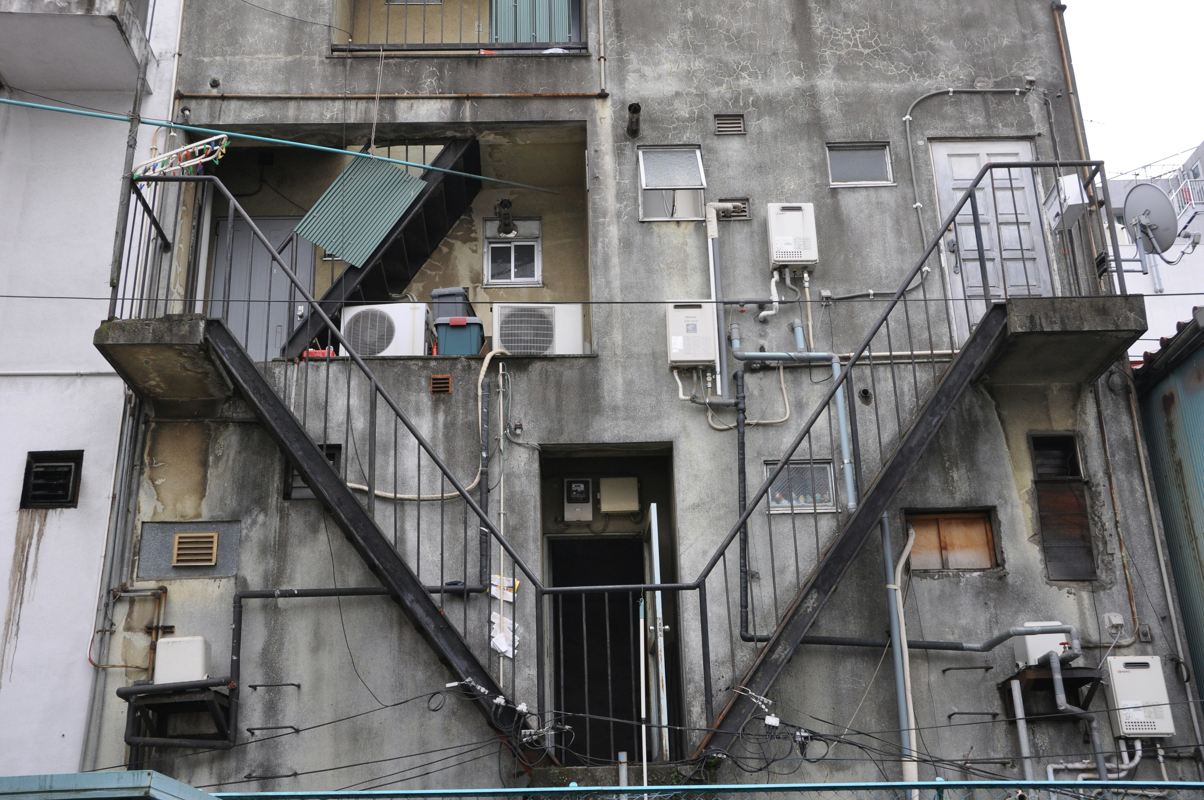 Vista trasera de un viejo edificio de concreto con escaleras de metal y unidades de aire acondicionado