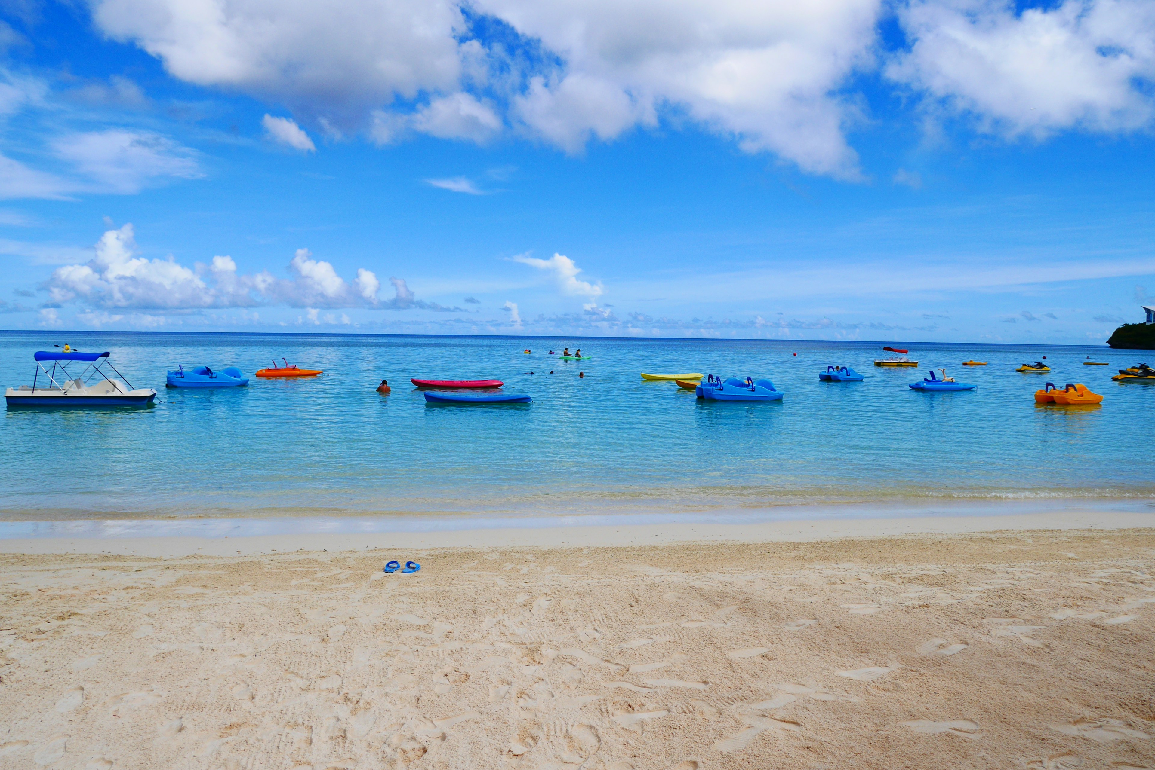 Pantai dengan perahu berwarna-warni mengapung di air biru jernih dan langit cerah