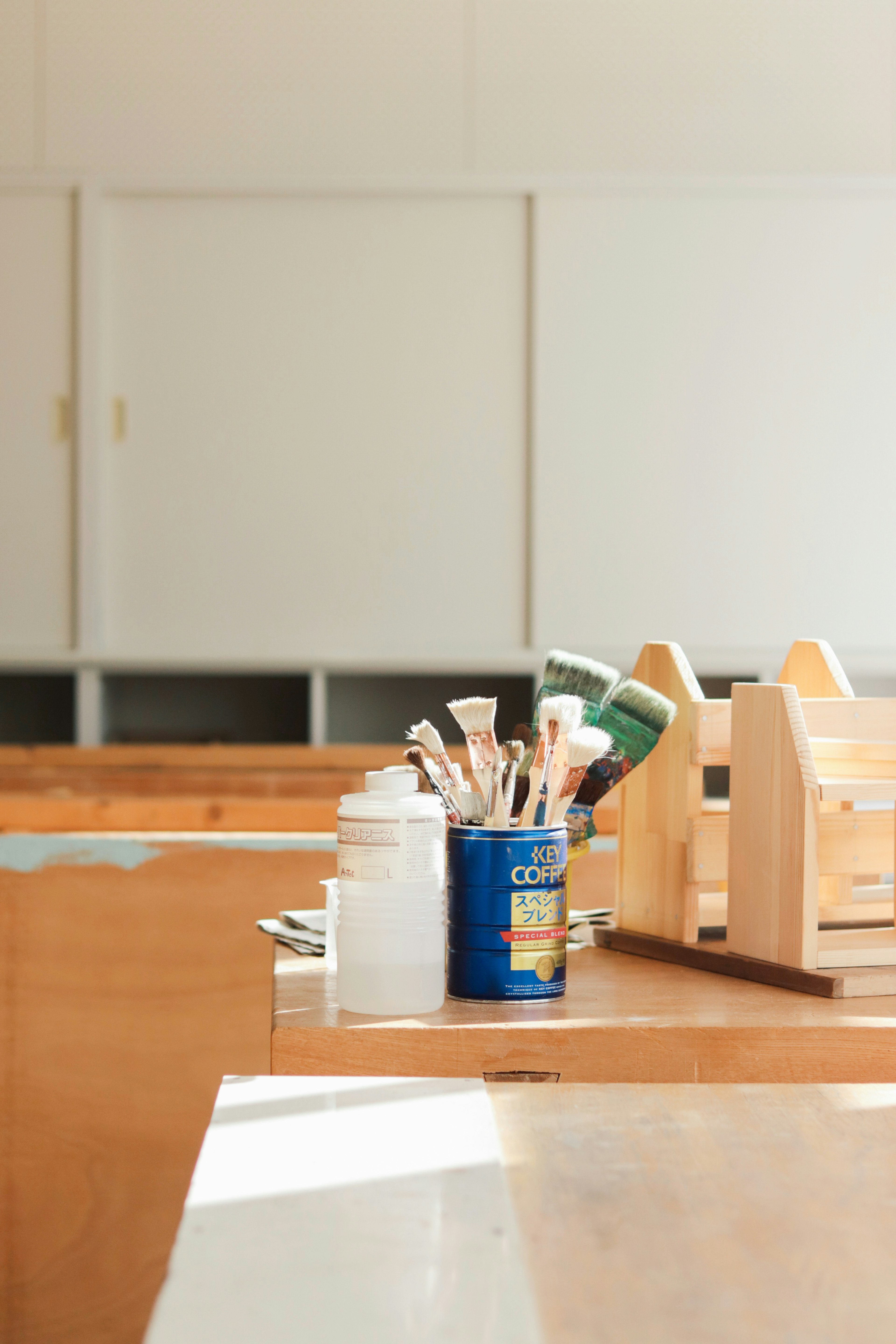 Des contenants de peinture et des pinceaux sur une table en bois avec une boîte à outils en bois à proximité contre un mur blanc