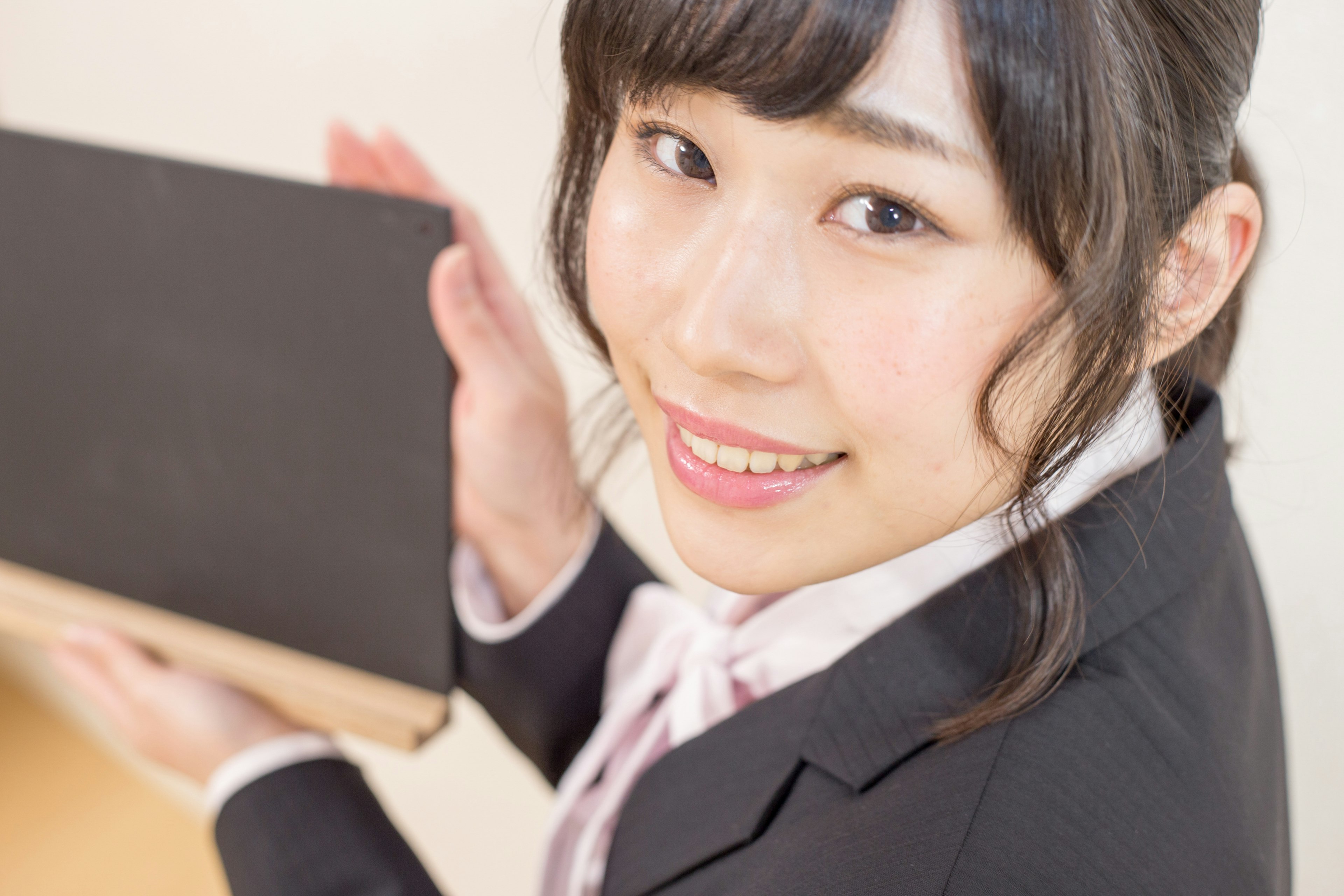 A woman in a business suit smiling while holding a black book