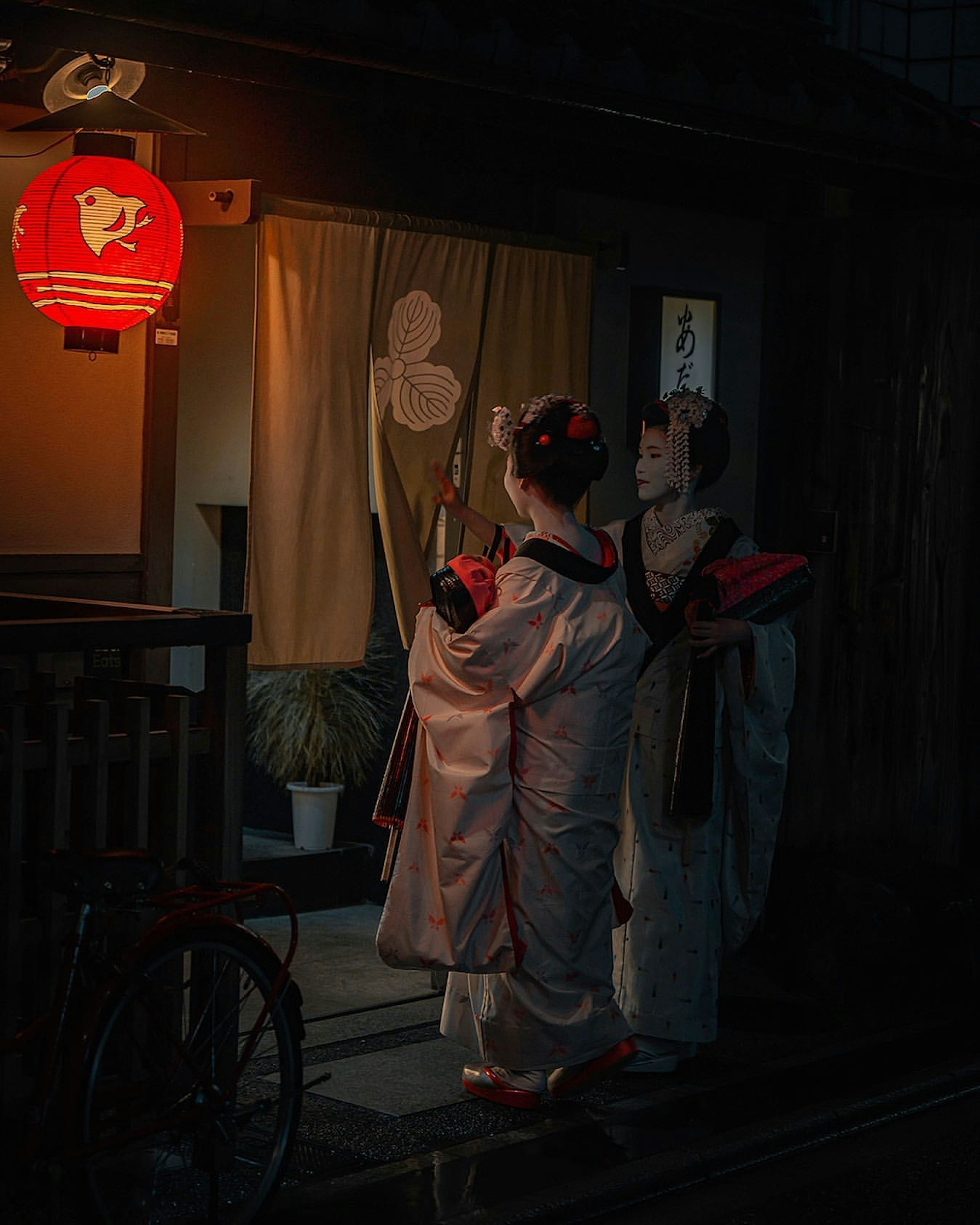 Two women in kimonos standing under a lantern in a nighttime street