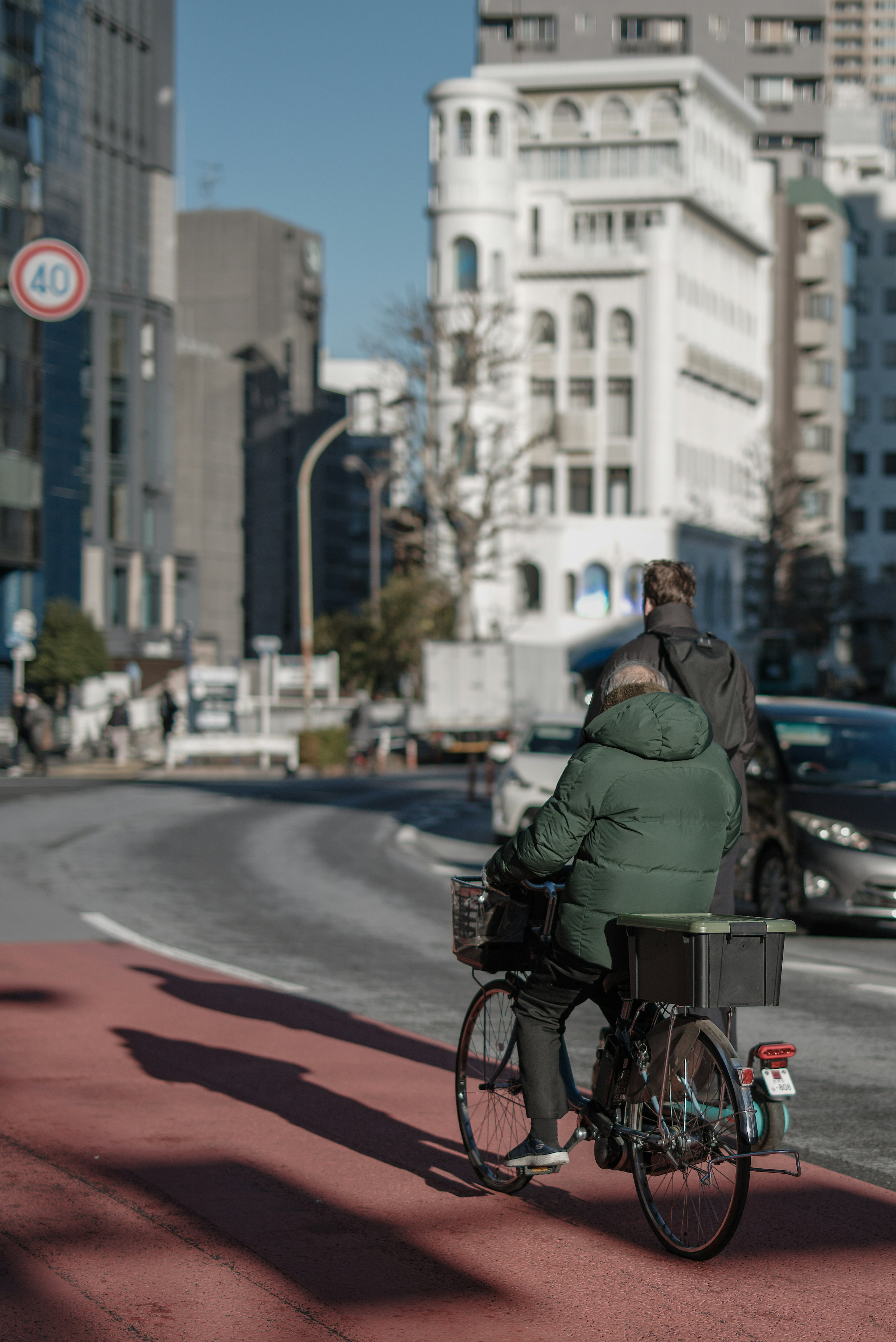 Persona in cappotto verde che pedala con sfondo urbano