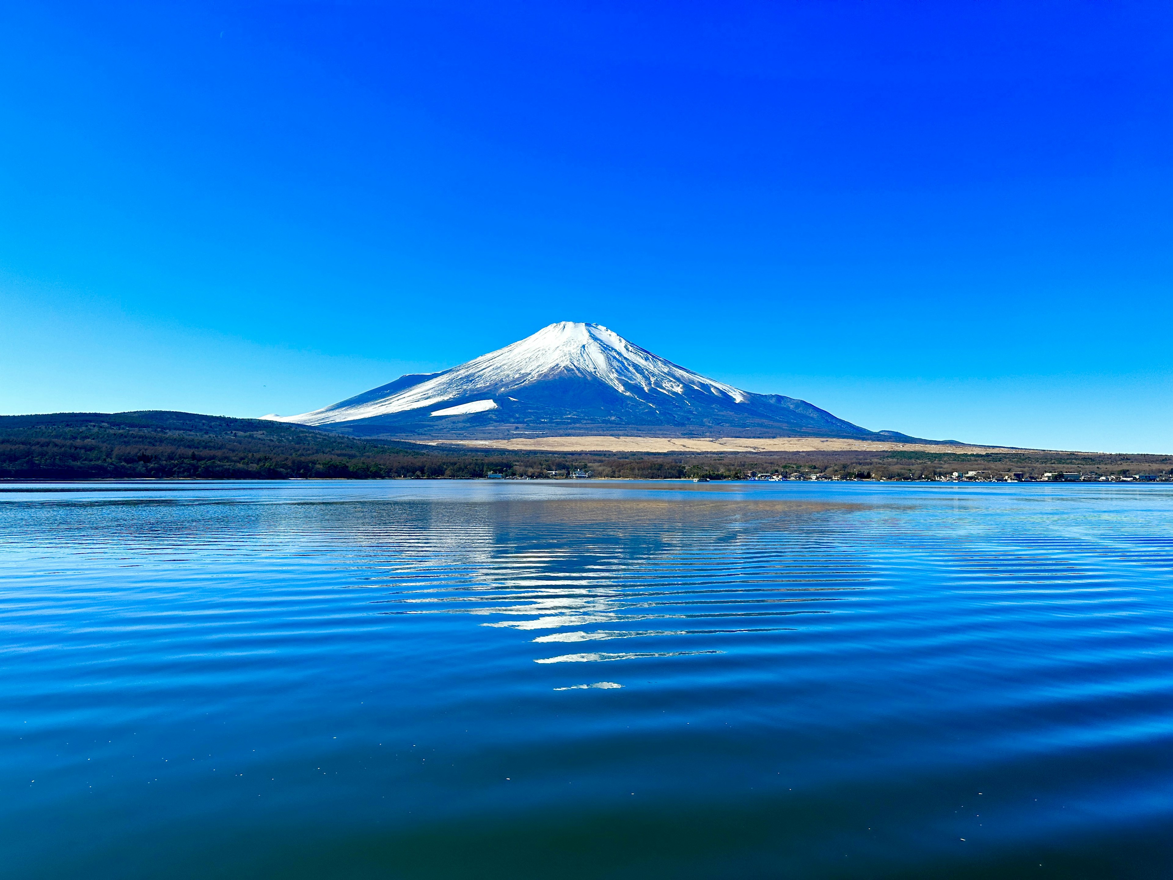 Monte Fuji elevándose bajo un cielo azul claro con su reflejo en la superficie del agua