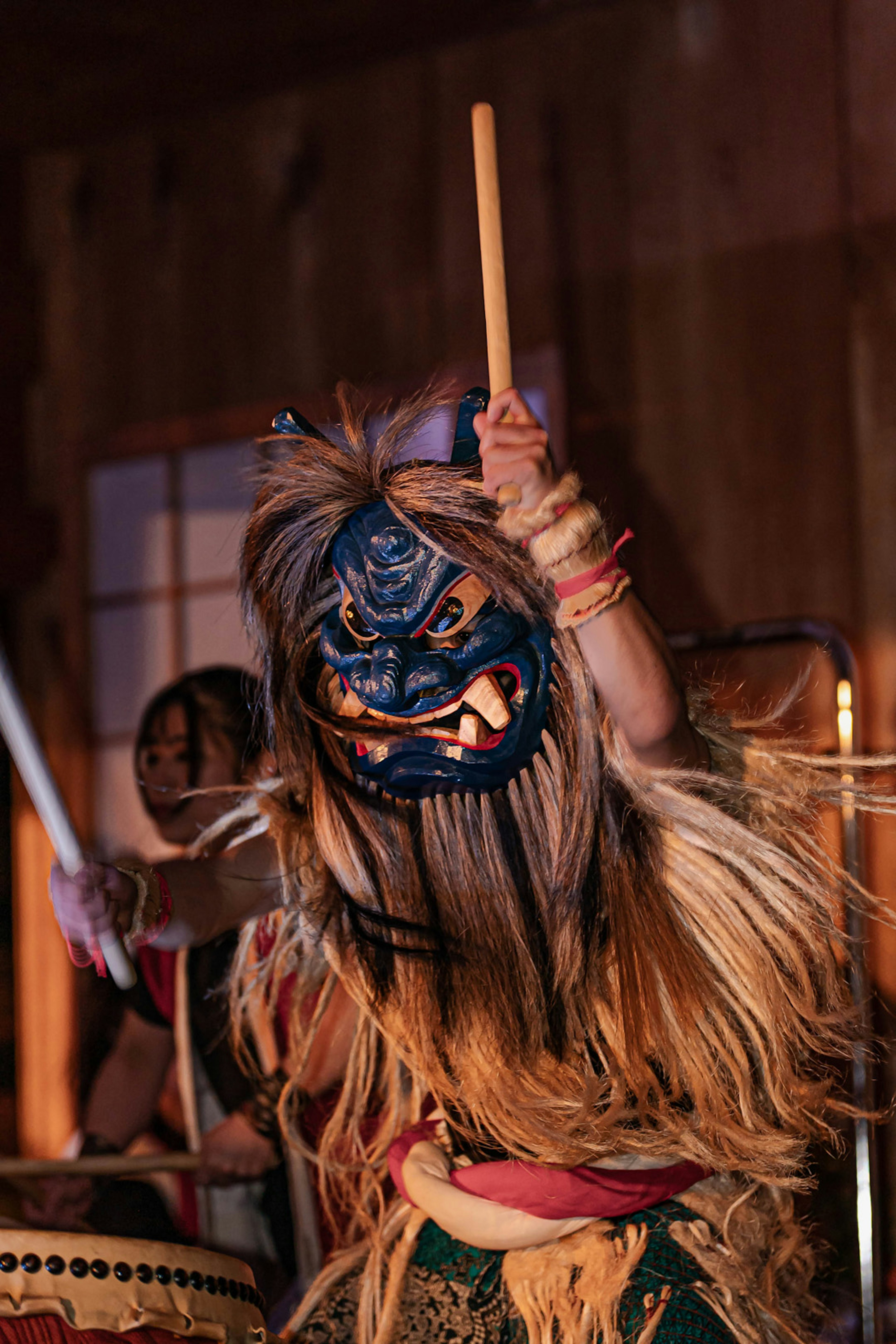 Performer wearing a traditional mask playing a drum