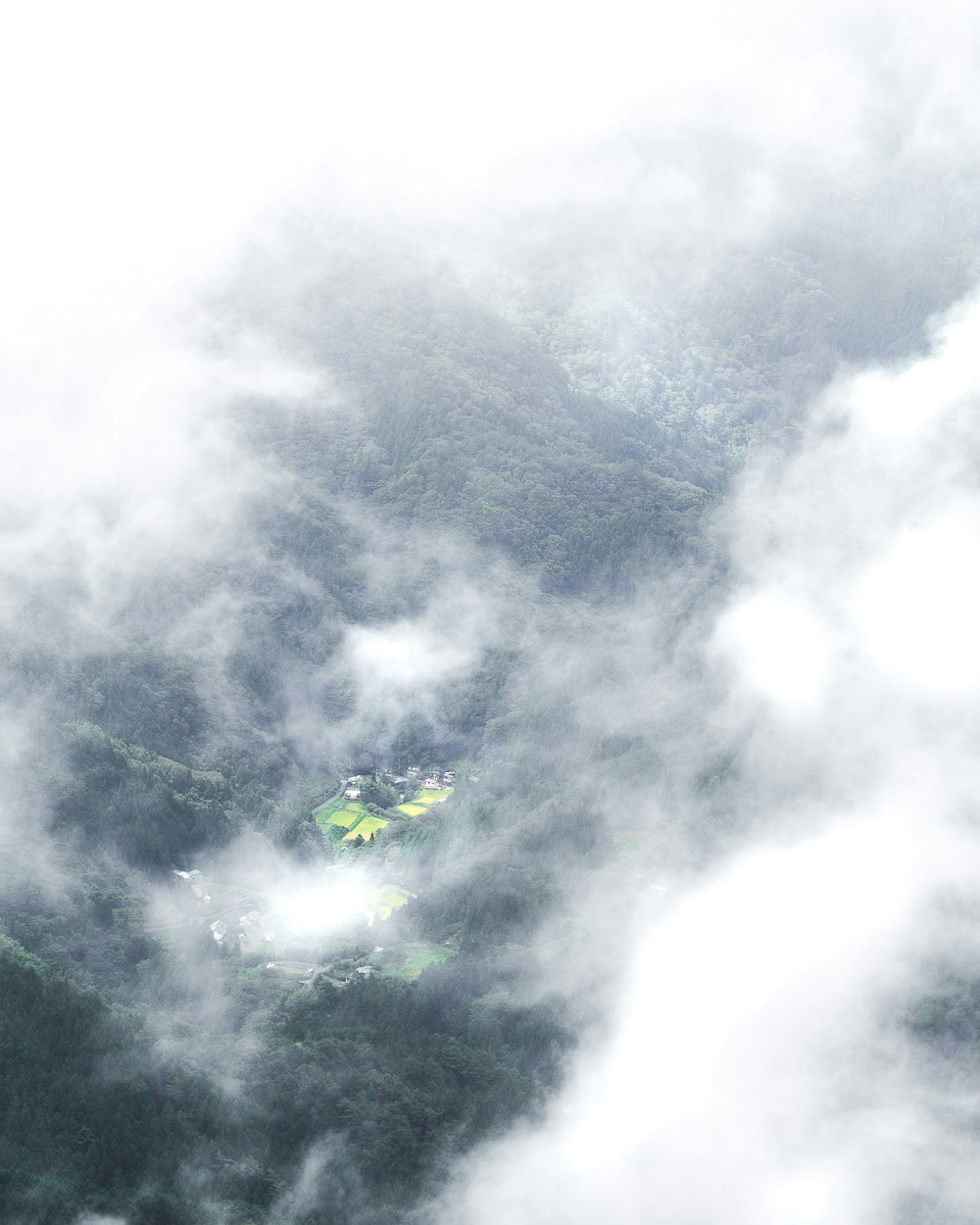 Aerial view of a small green field surrounded by dense clouds and mountains