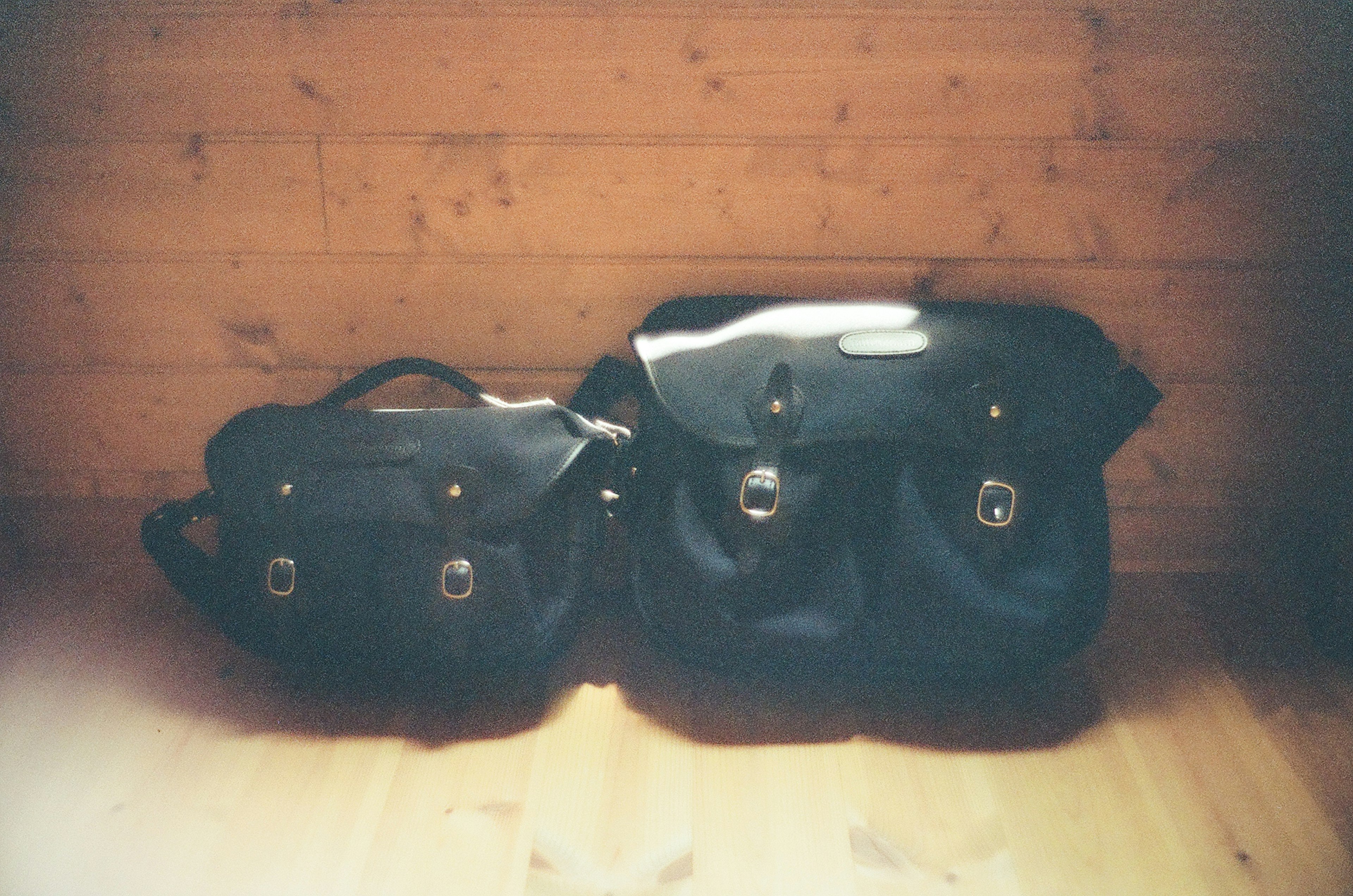 Two black bags positioned in front of a wooden wall