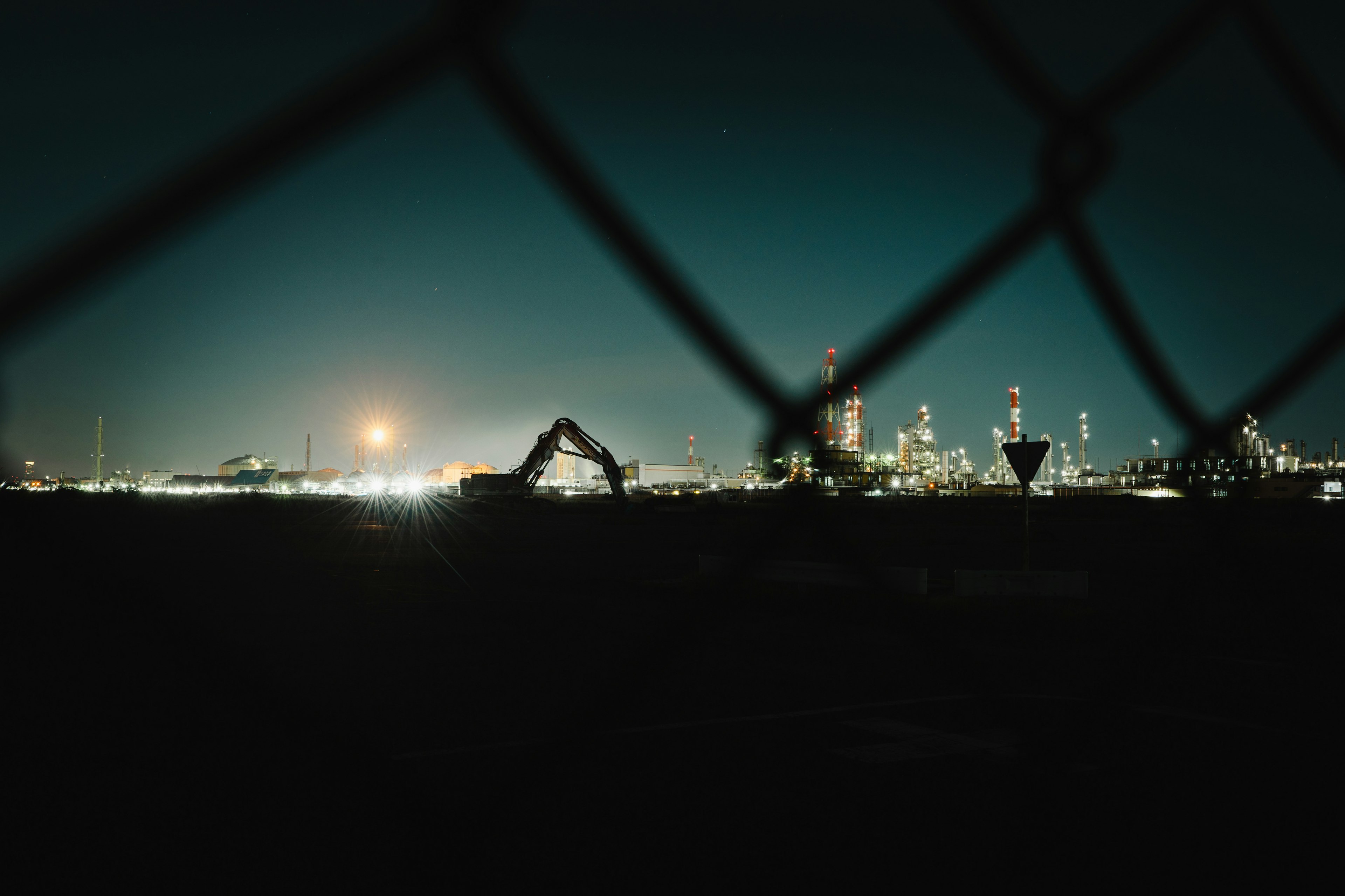 Night view of an industrial area behind a fence with city lights