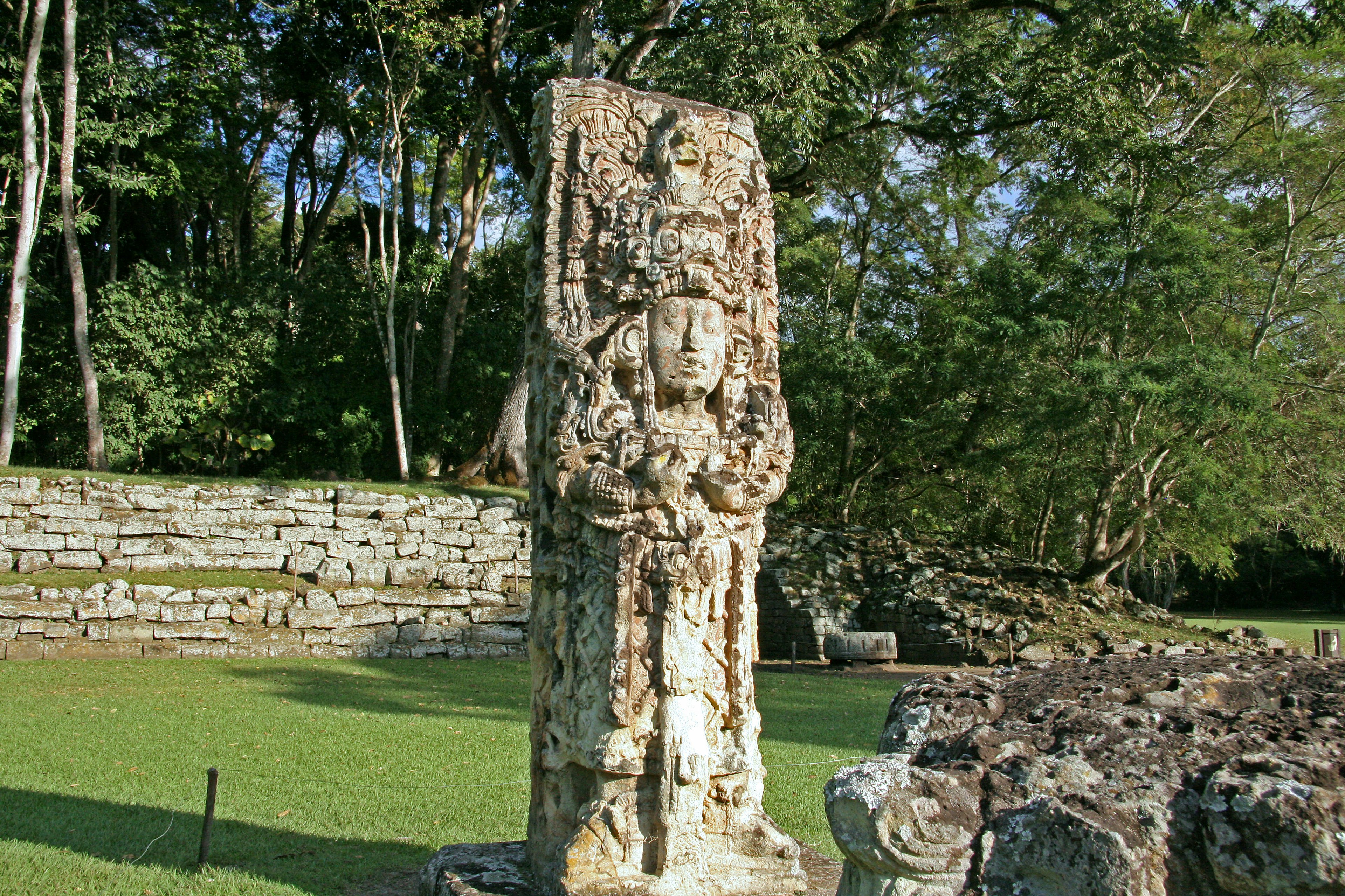 Scultura antica che si erge in un sito archeologico lussureggiante