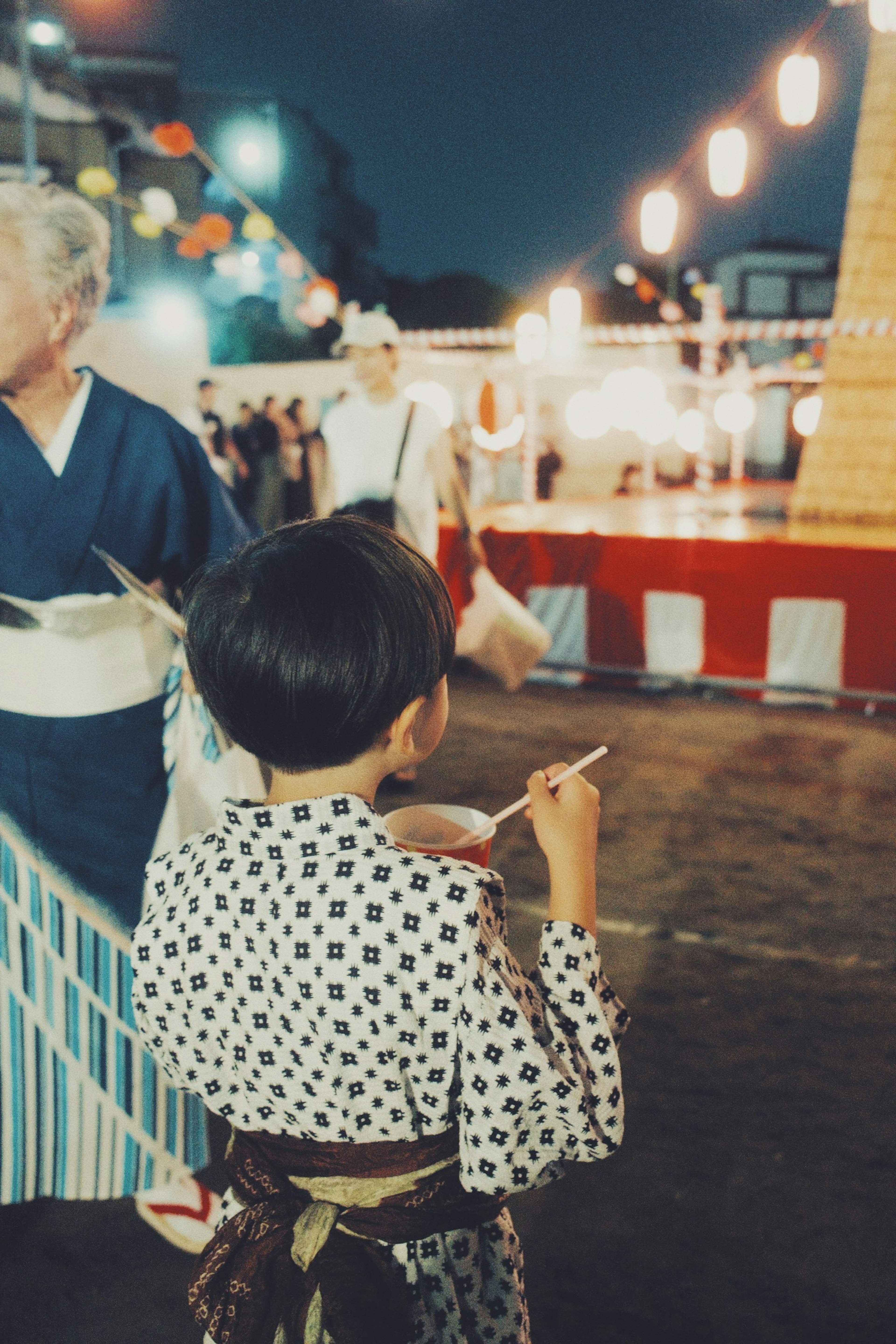 Child in a yukata holding food at a night festival