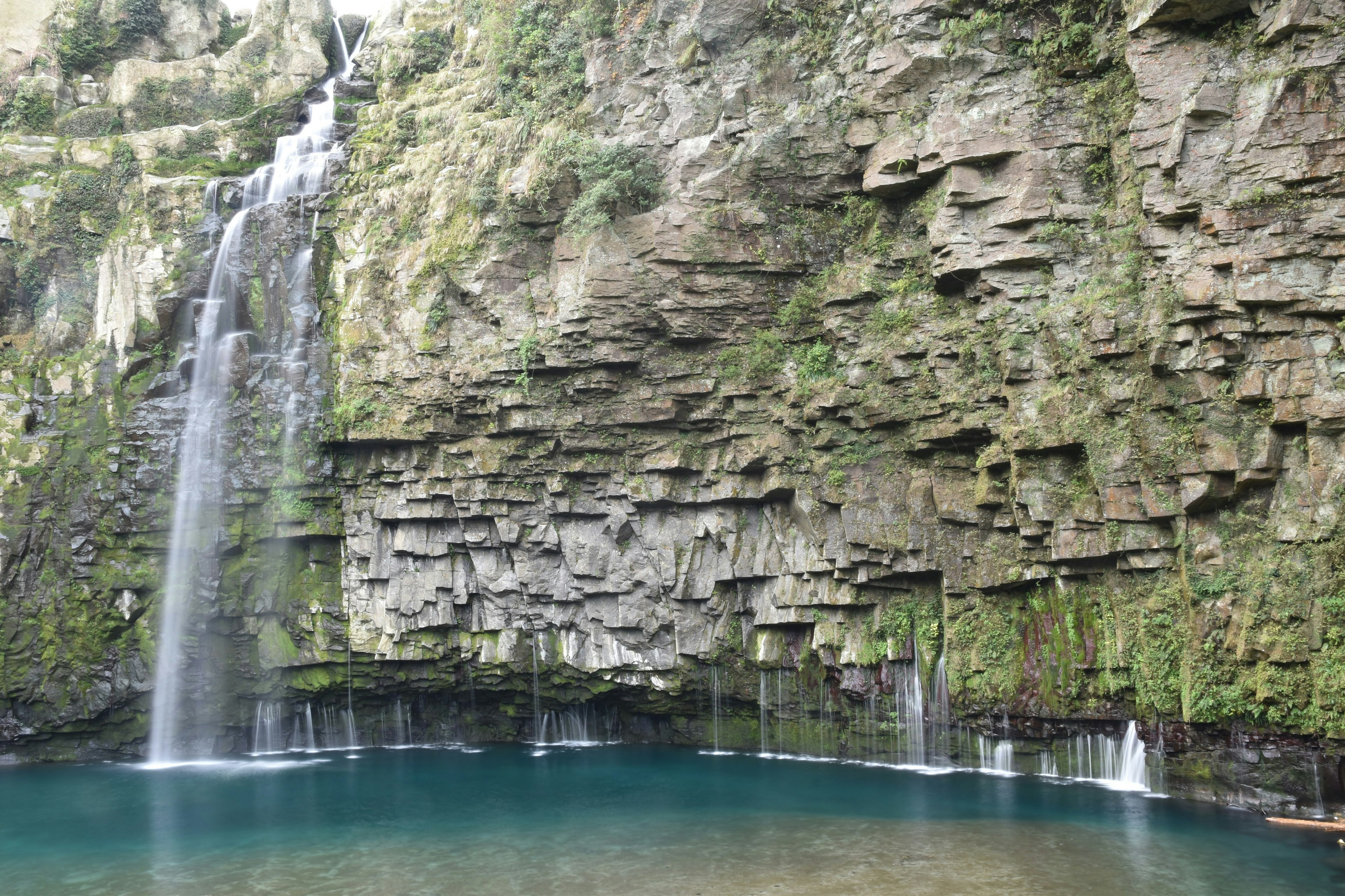 Ein schöner Wasserfall, der von einer felsigen Klippe in einen ruhigen blauen Pool fällt, umgeben von grünem Moos